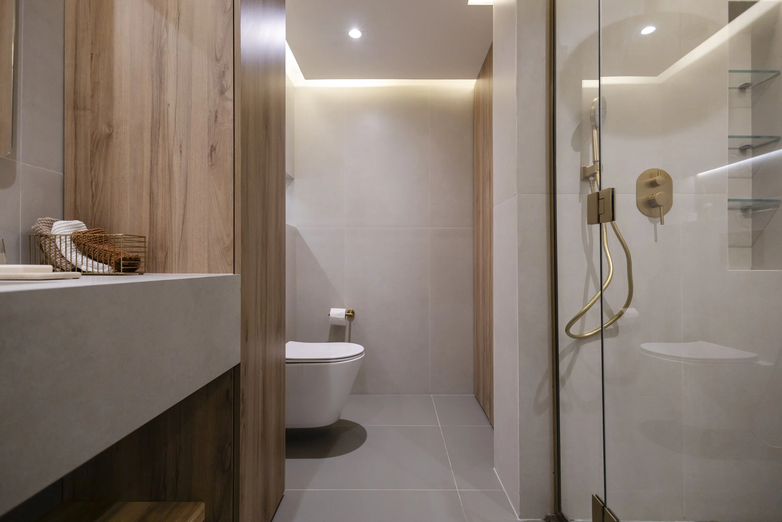 Modern bathroom with wooden accents, a toilet, a glass shower with gold fixtures, and a minimalistic design.