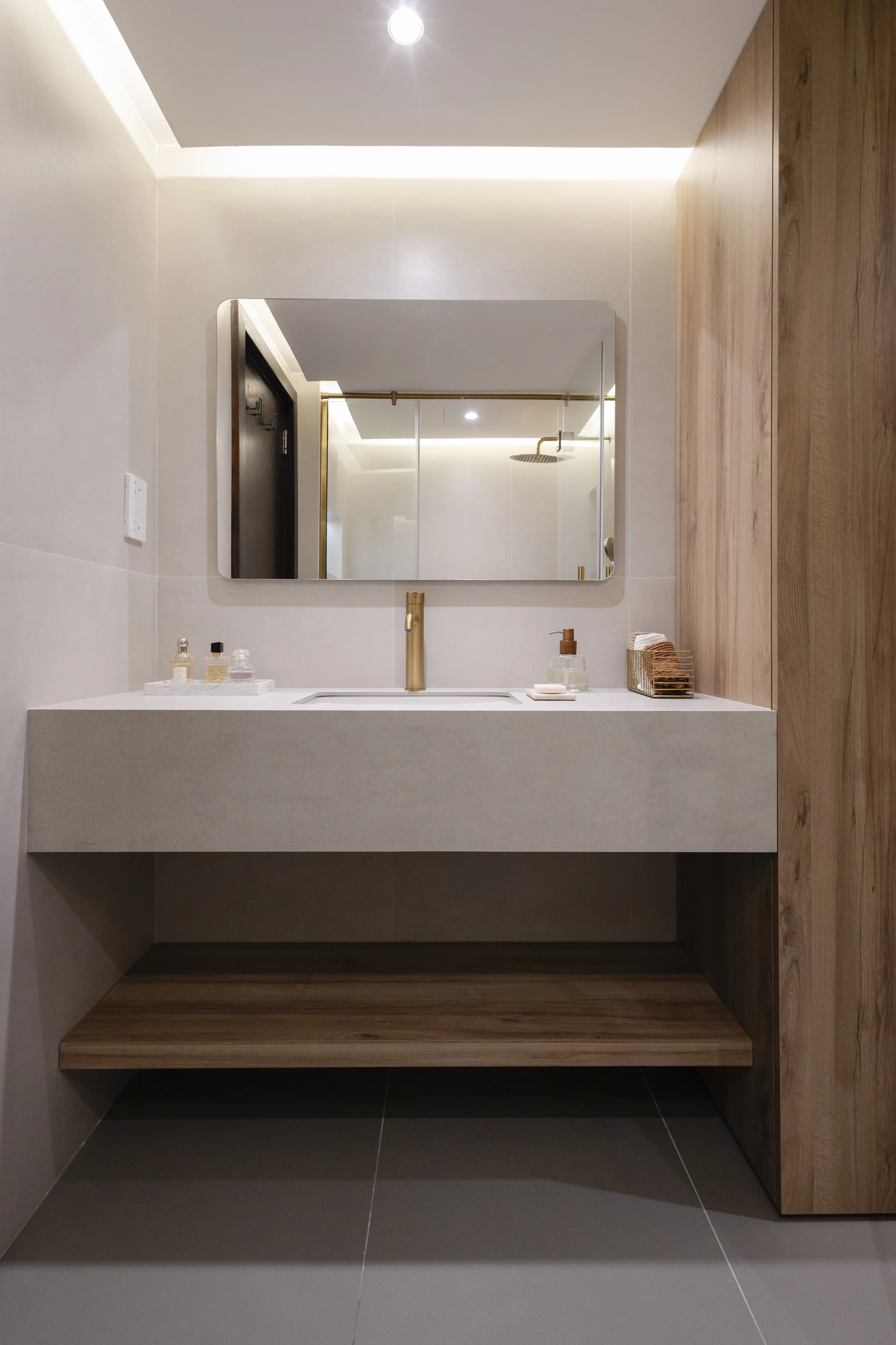 Modern bathroom with a rectangular sink and gold faucet, mirror above, wood paneling on the right, and small toiletries on the sink.