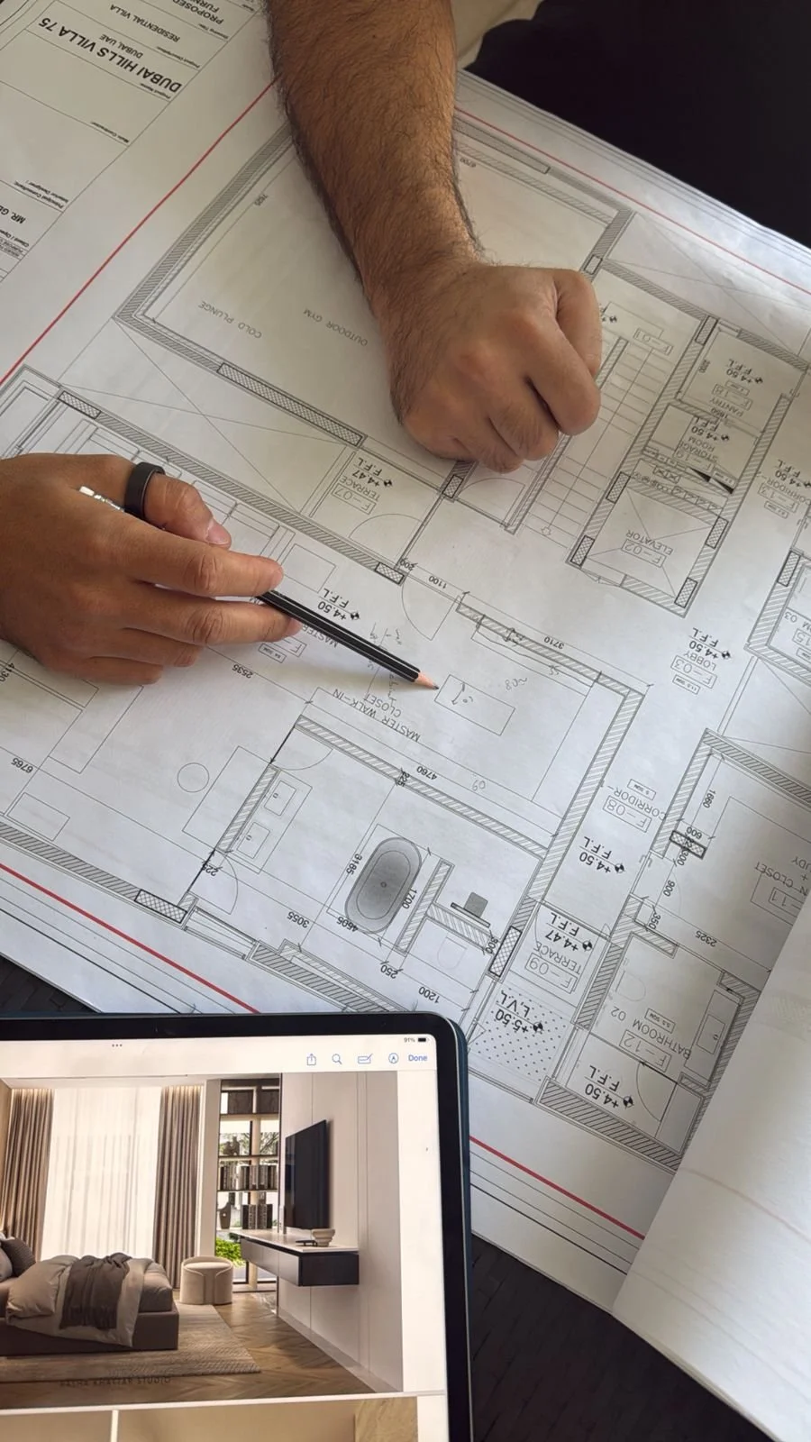 People reviewing architectural blueprints and interior design plans on a table, with a tablet displaying a living room photograph.
