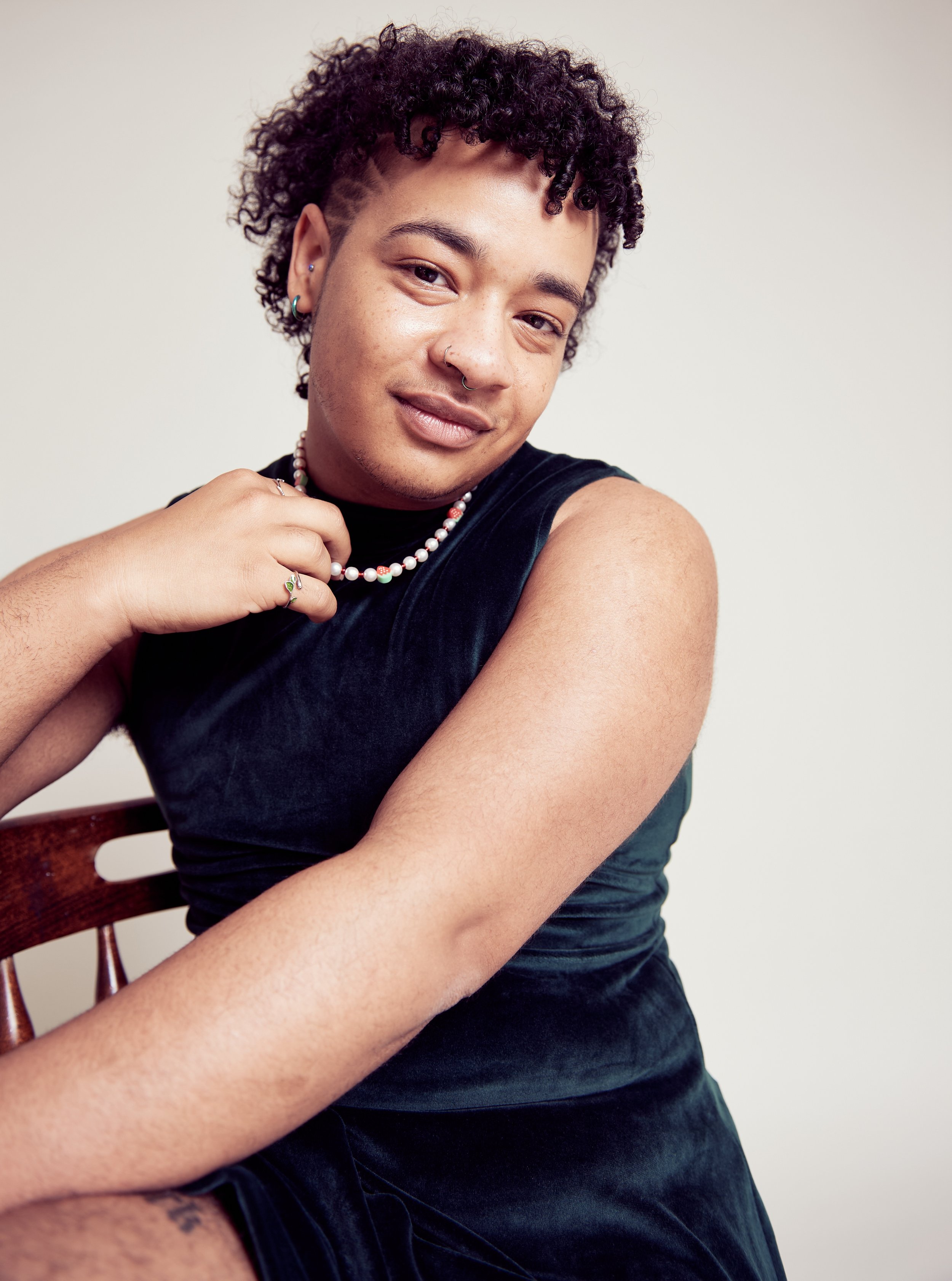 a lighter skinned black person in a green velvet dress siting on a chair and smiling