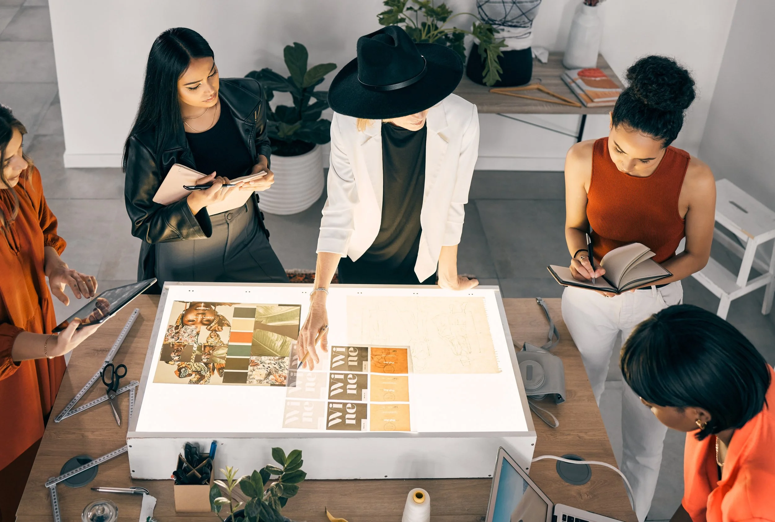 Group of people collaborating on a design project around a lightbox table, examining prints and taking notes.