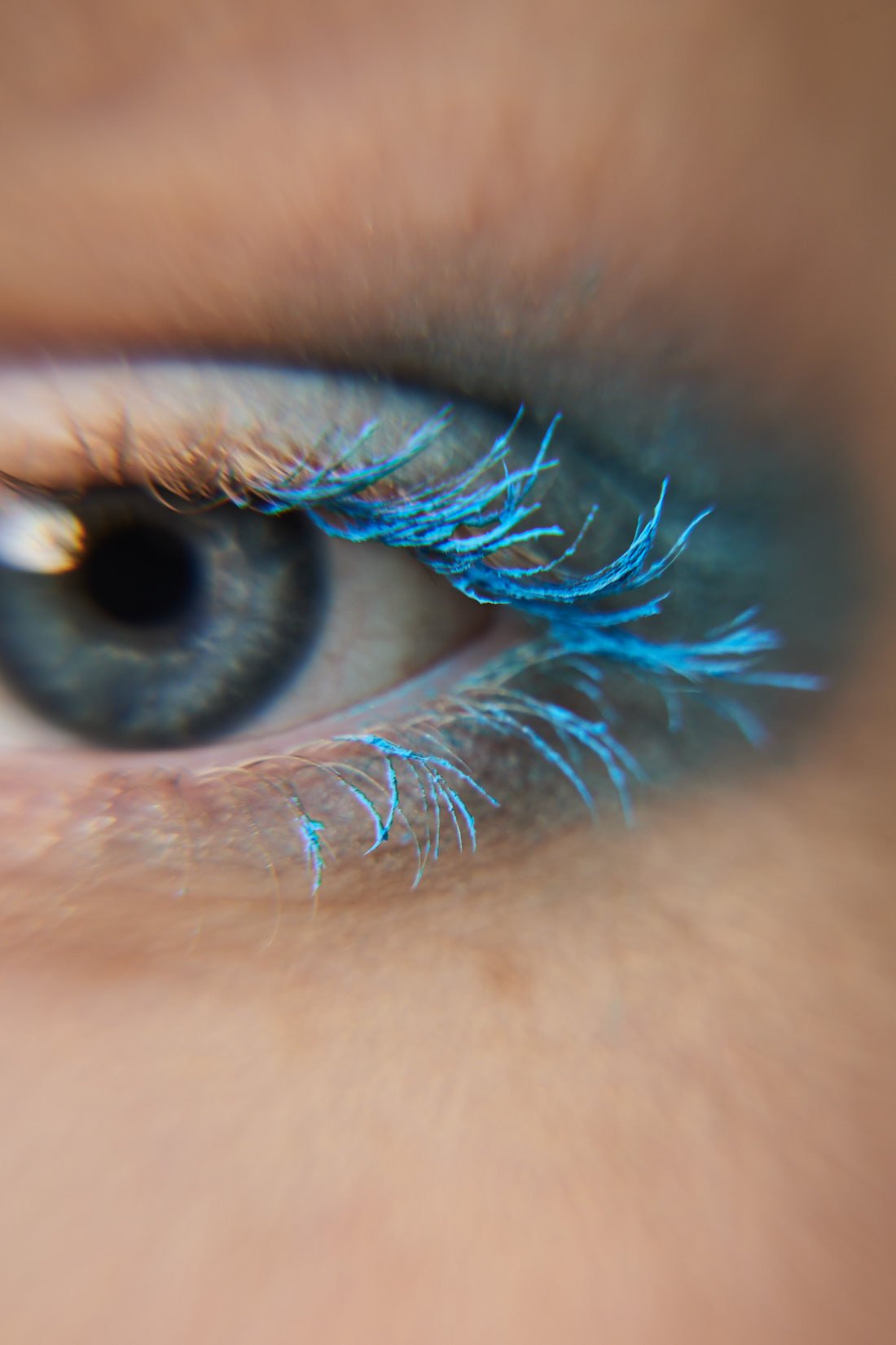 Close-up of a person's eye with blue eyeshadow and long eyelashes.