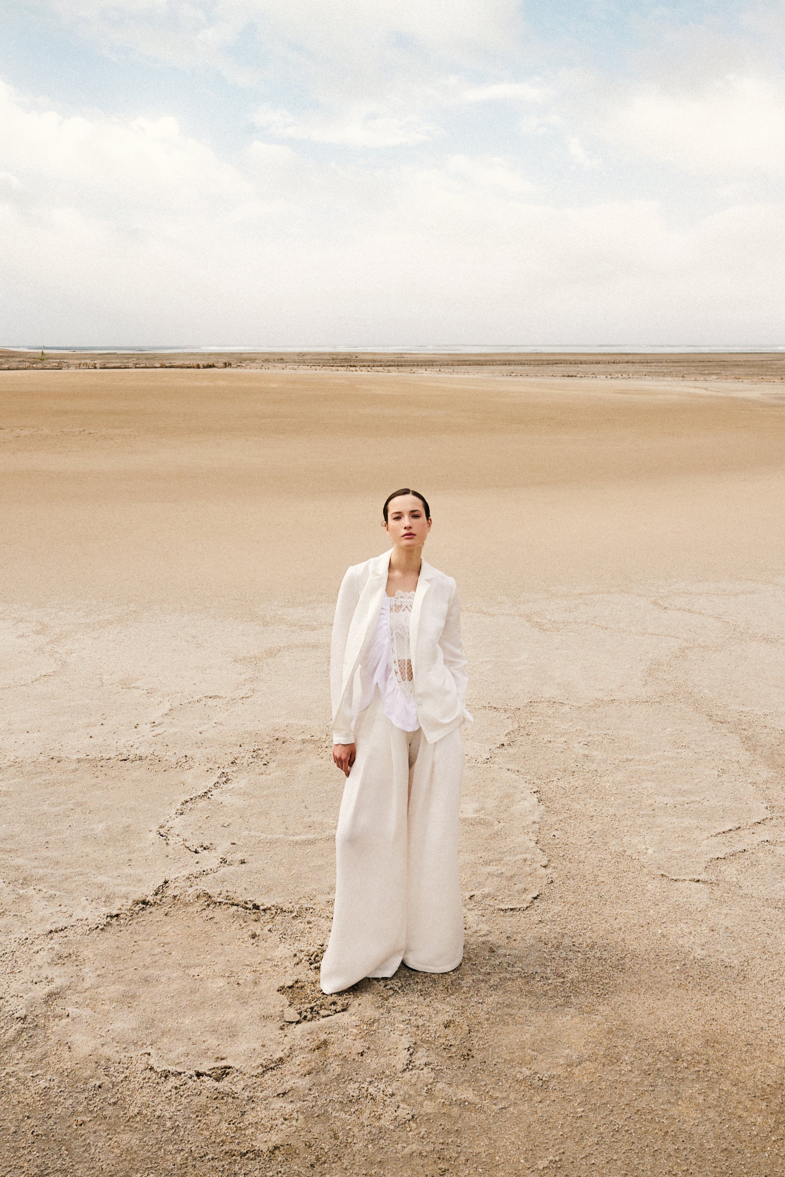 A woman dressed in white standing on a vast, sandy desert landscape under a cloudy sky.