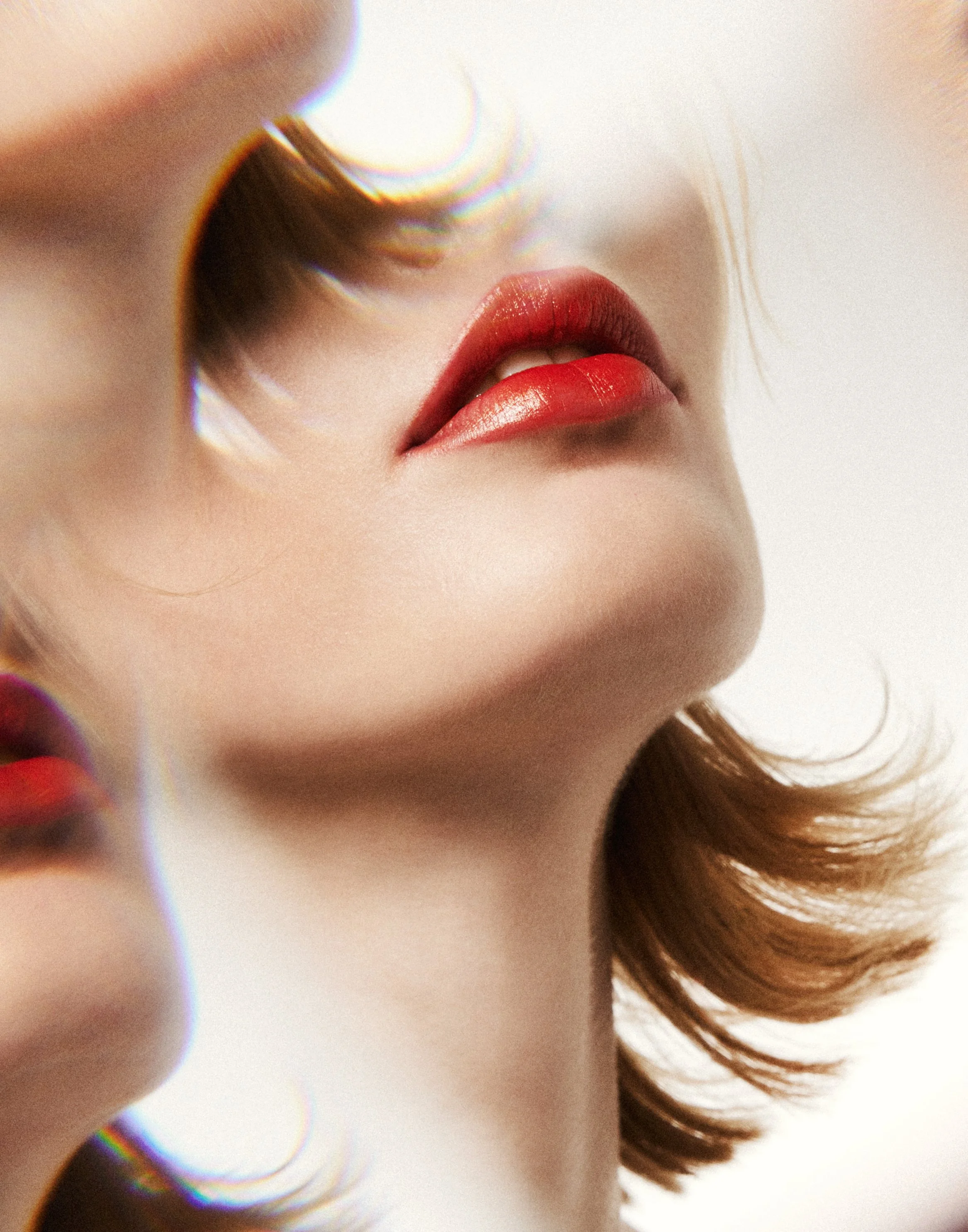 Close-up photo of a woman's lips painted with red lipstick, with blurred hair and a bright background.