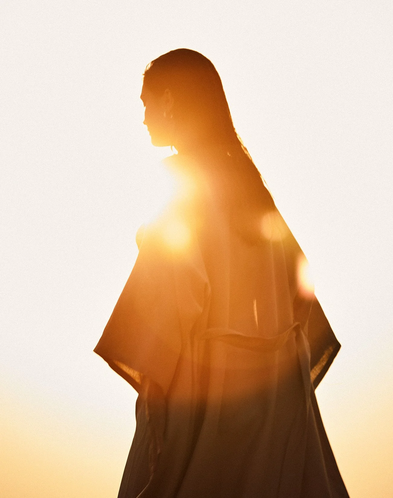 Silhouette of a person with long hair looking down against a bright, sunlit background.