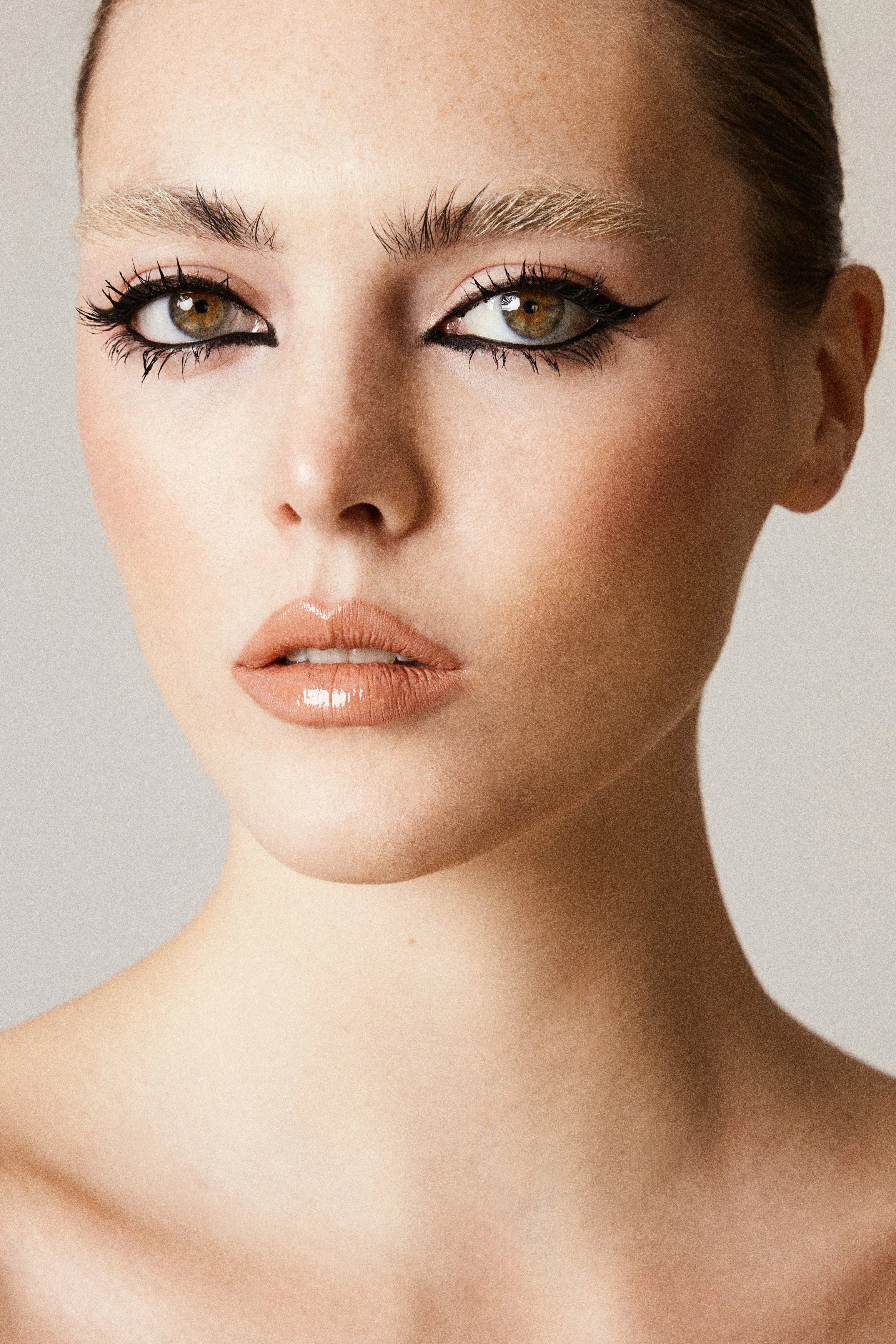Close-up of a woman's face, showing her eyes, eyebrows, nose, and lips with makeup and glossy lips.