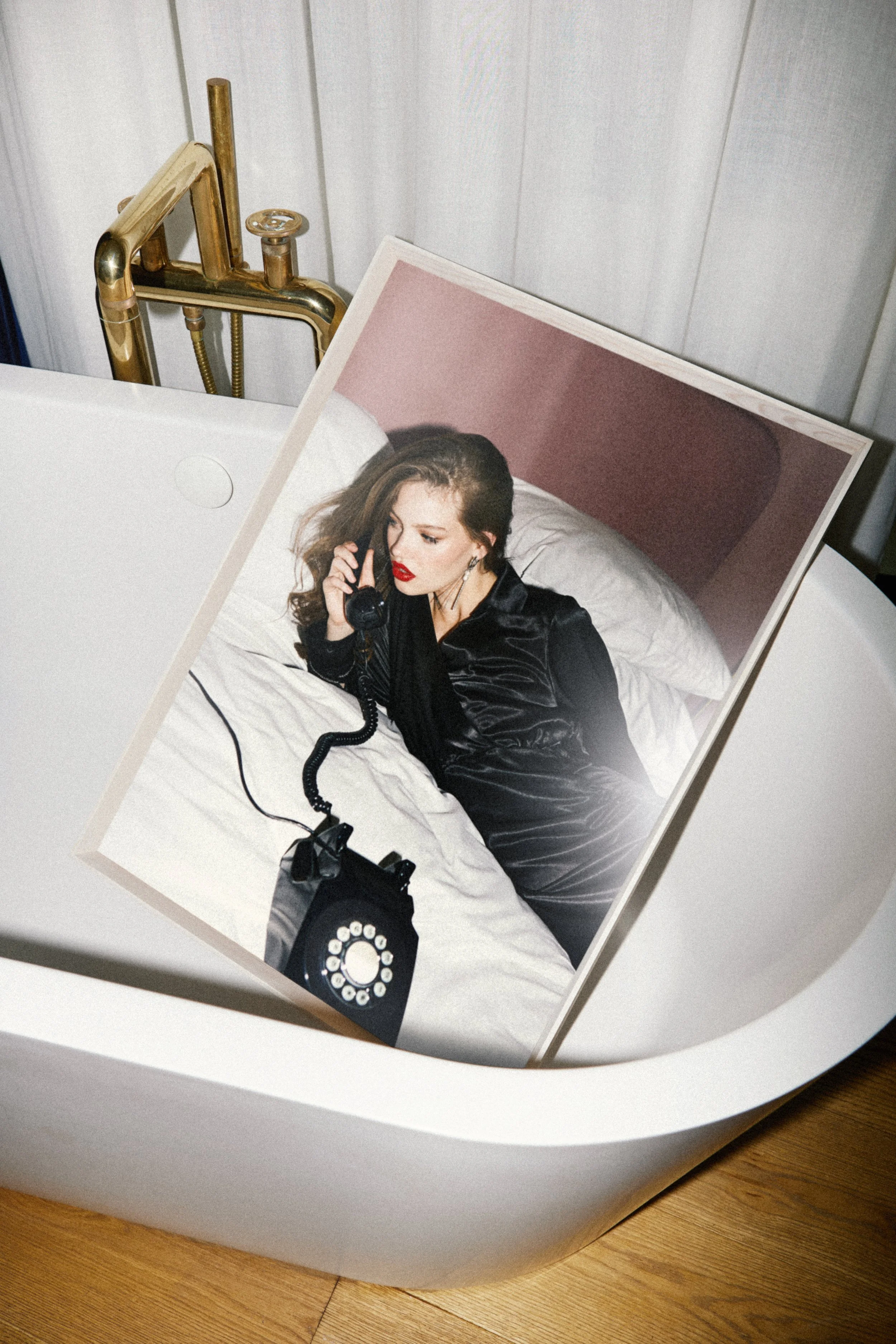 A photograph of a woman with dark hair and red lipstick lying in a bed, speaking on the phone. The image is printed on a panel inside a white, oval-shaped device, which is placed on a wooden floor.