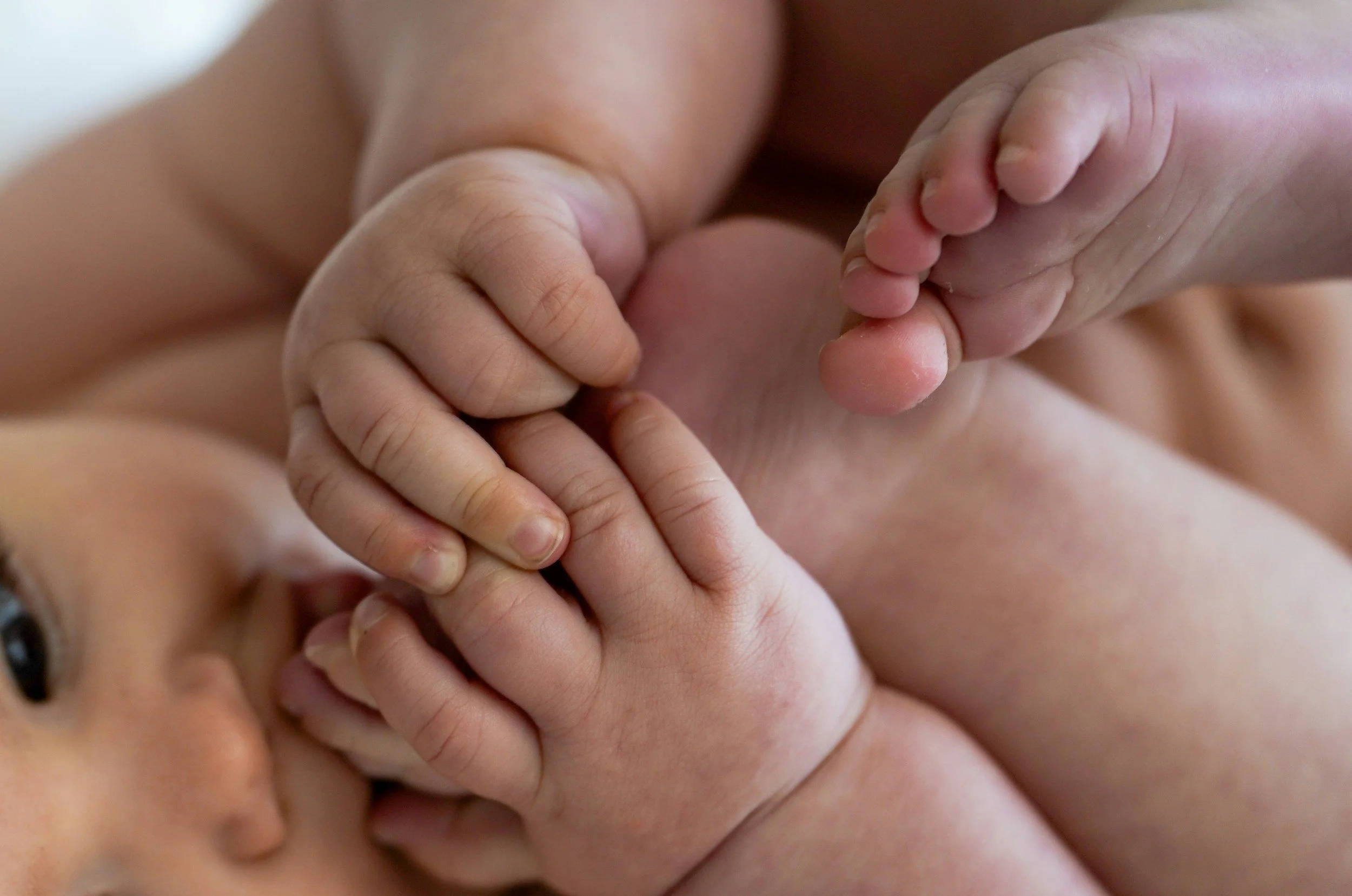 A close-up of a baby holding an adult's finger with both hands.