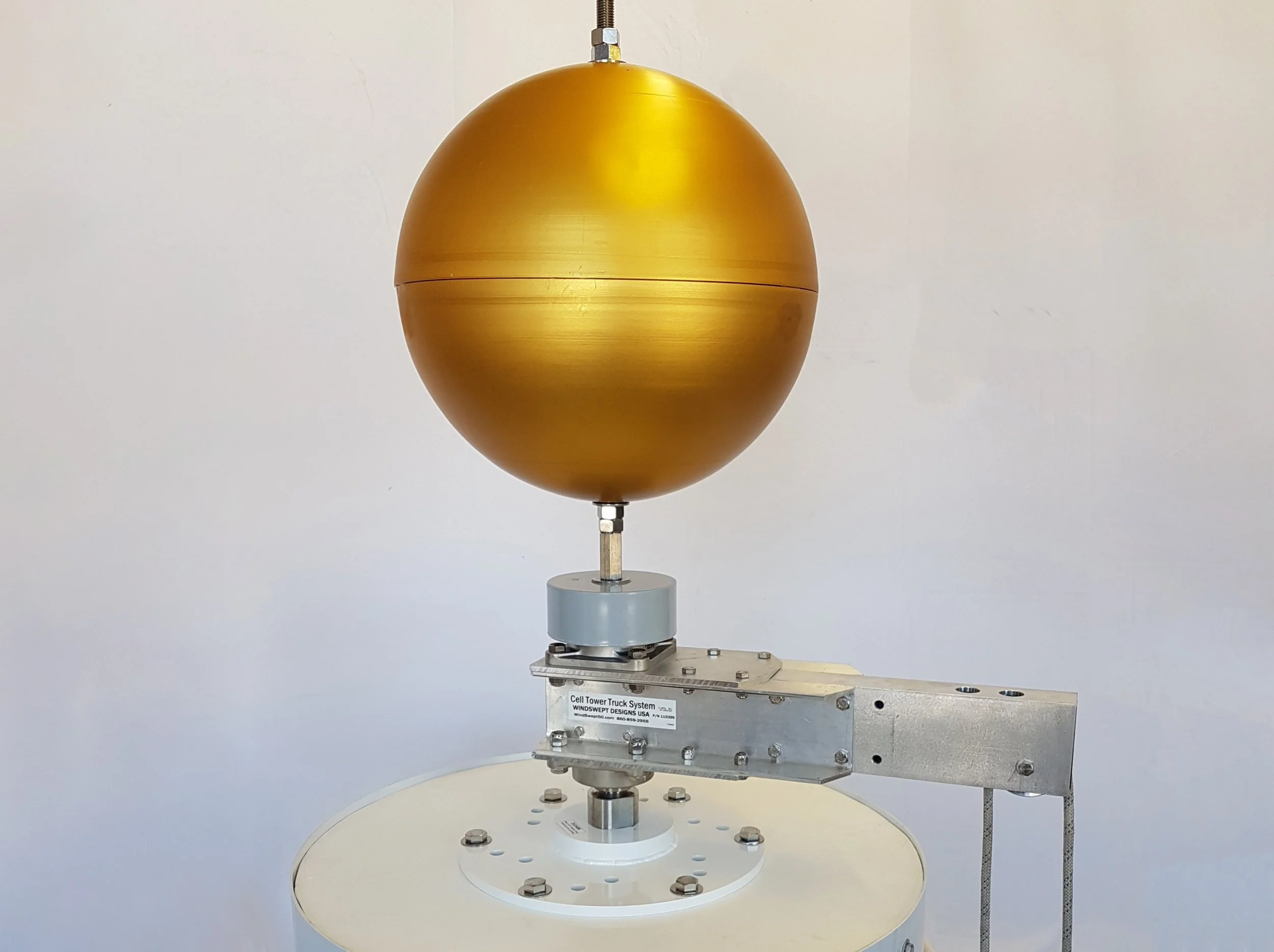 The top of a cell tower with an Adapter Plate, SwingArm Truck, Finial Ball, Halyard, and American Flag against a blue sky.