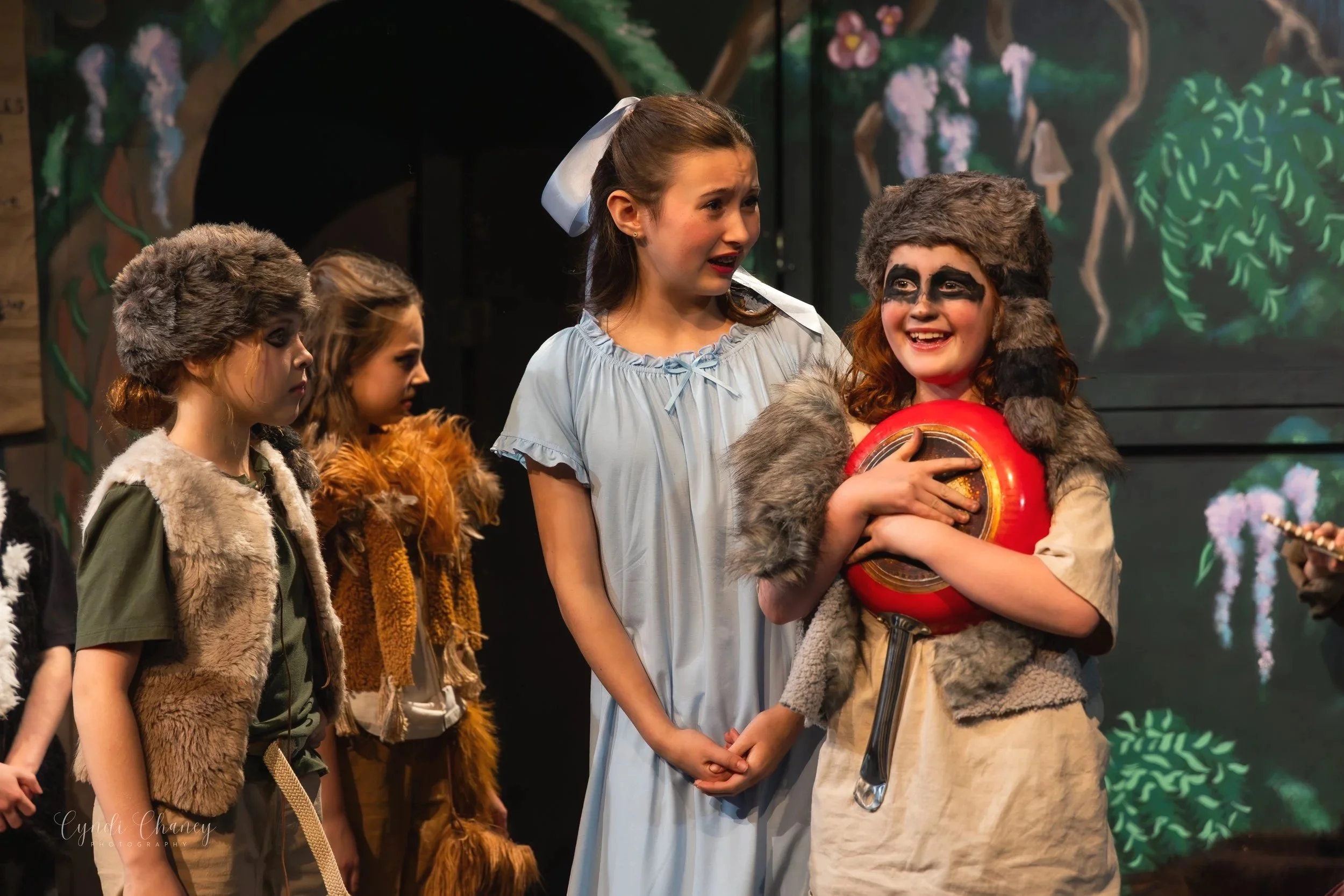 Three children dressed in fur caps as Lost Boys in Peter Pan and a girl with a blue nightgown and big blue bow dressed as Wendy from Peter Pan