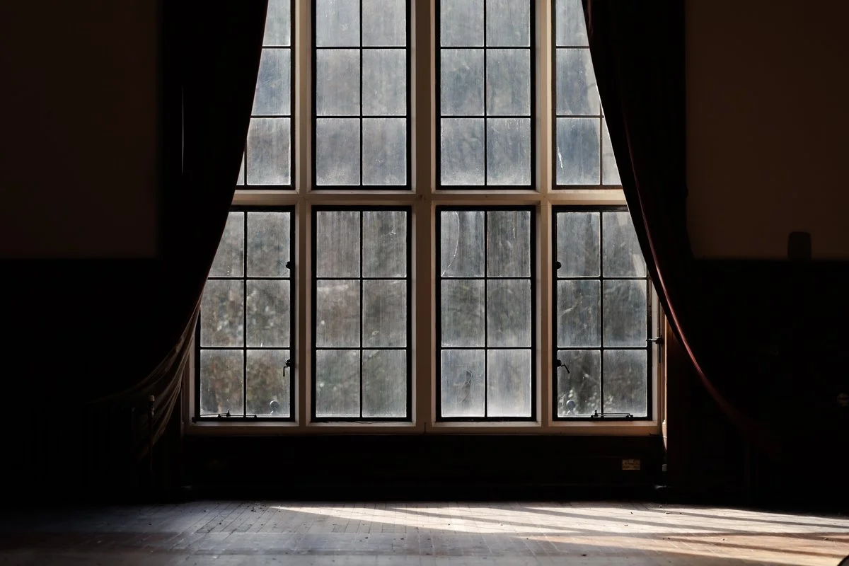 A large window with multiple panes, flanked by dark curtains, letting in natural light and revealing an outdoor scene with trees.