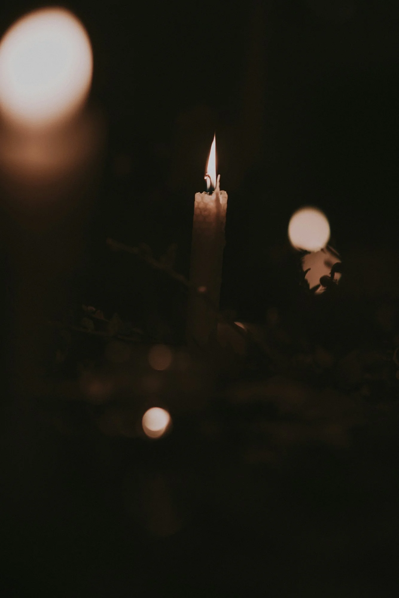 A lit candle in darkness with blurred lights in the background.
