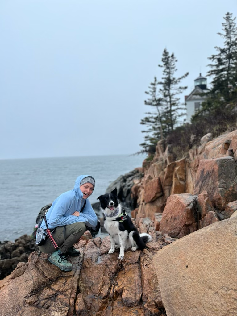 A woman and her border collie posing for a picture on the coast of Maine in Acadia National Park 
