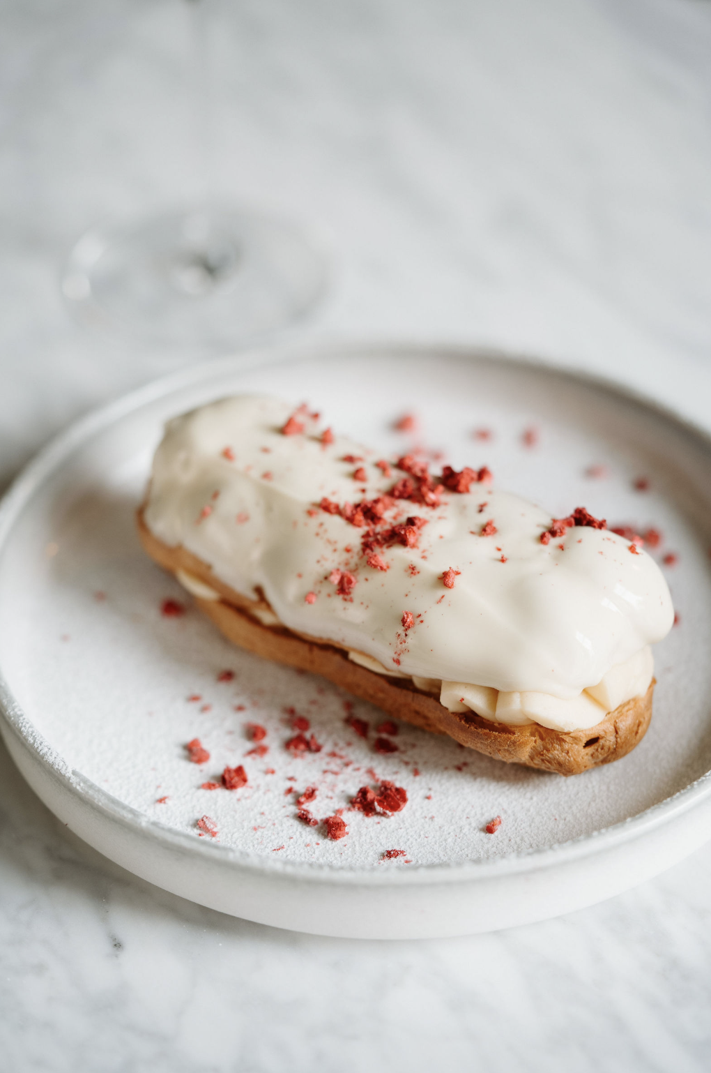 A cream-filled éclaire topped with white icing and red sprinkles on a white plate.