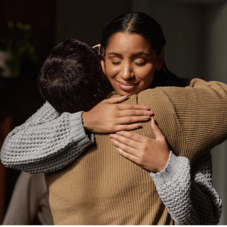 A woman hugging another person with a hopeful smile