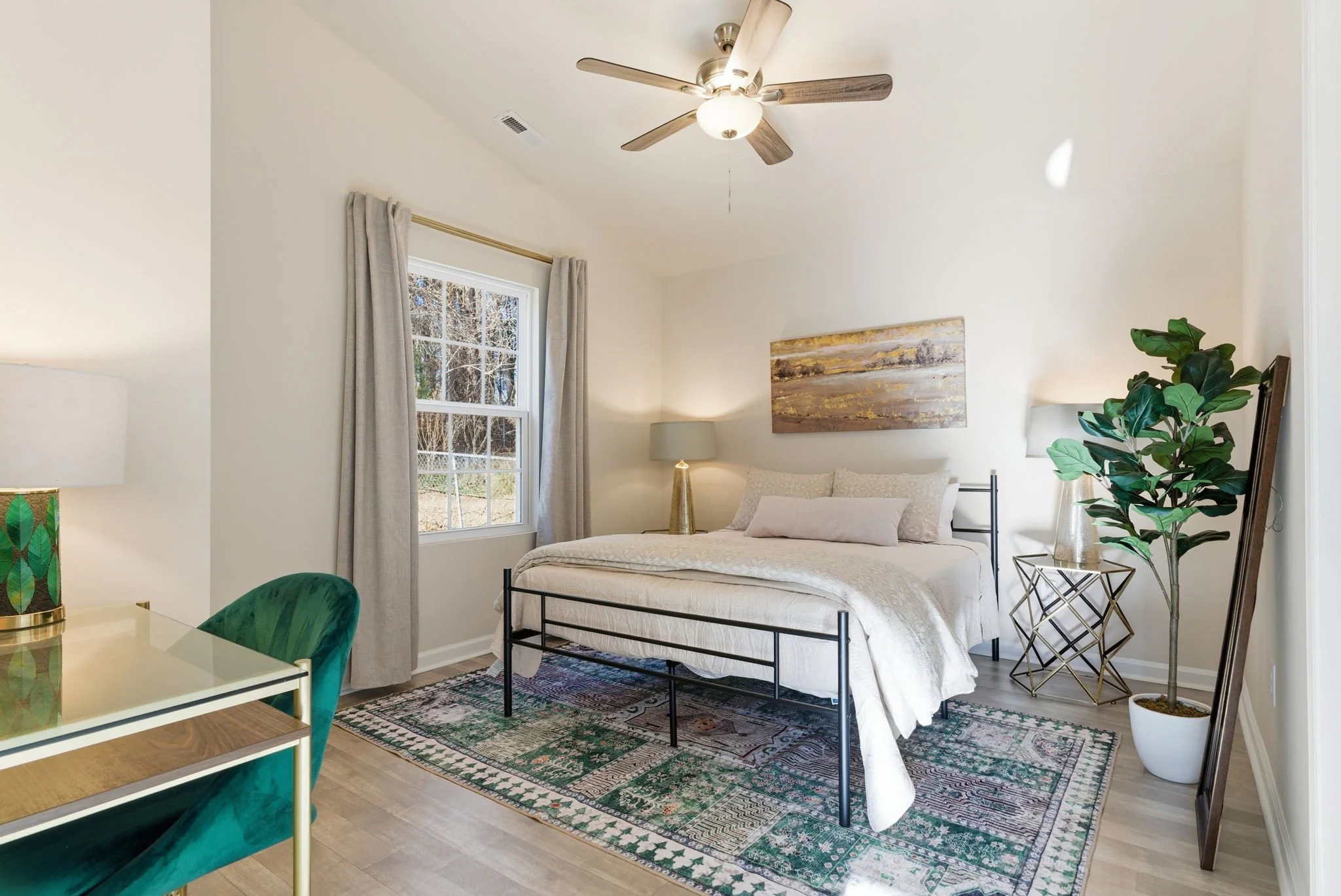 Stylish second en suite bedroom with a green velvet accent chair, faux fiddle-leaf fig, and a gold-framed desk. A perfect work-from-home setup for travel nurses and relocation guests.