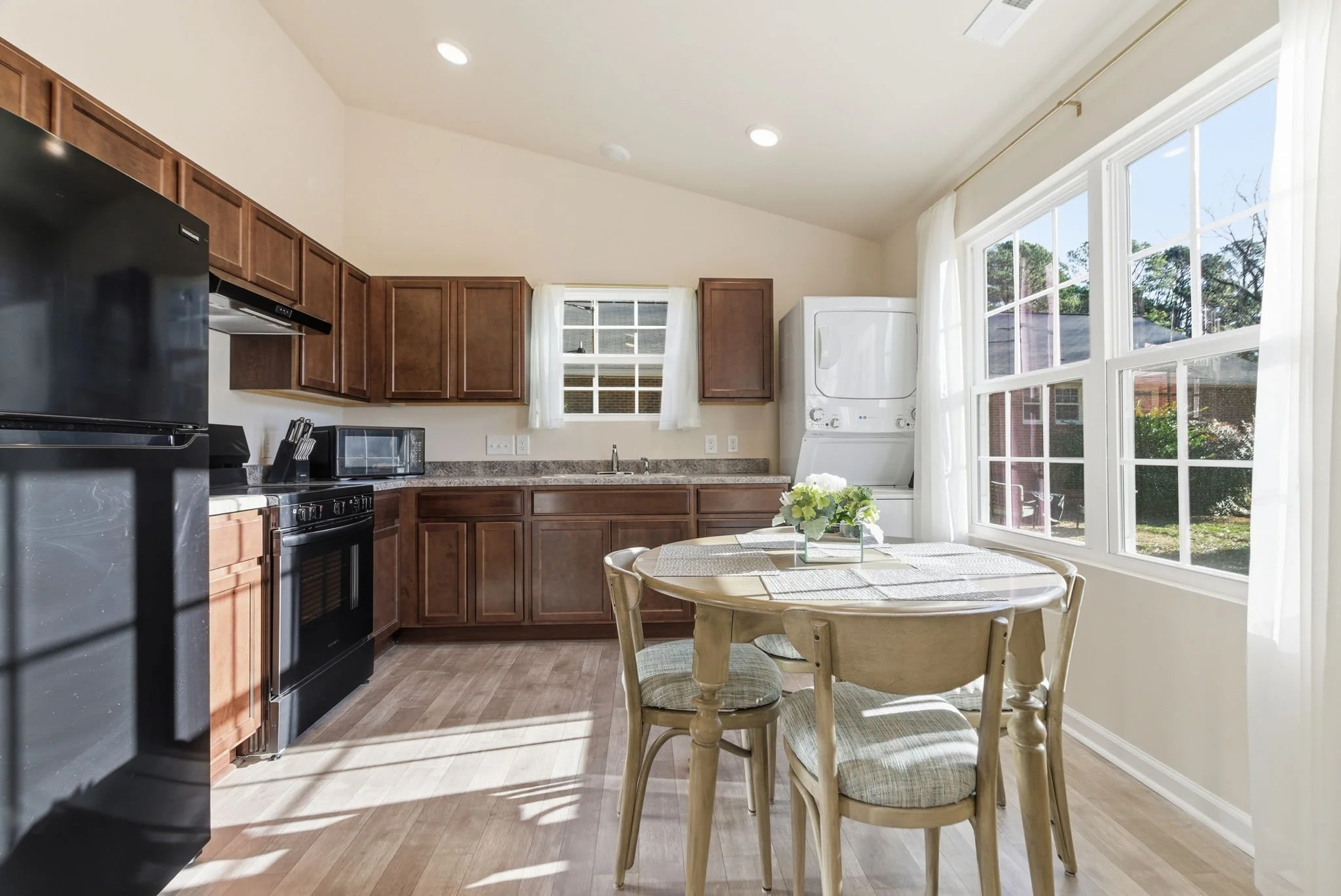 Fully equipped chef’s kitchen with dark wood cabinetry, black appliances, and a dedicated dining area. Features a convenient in-unit stacked washer and dryer for long-term or mid-term stays.