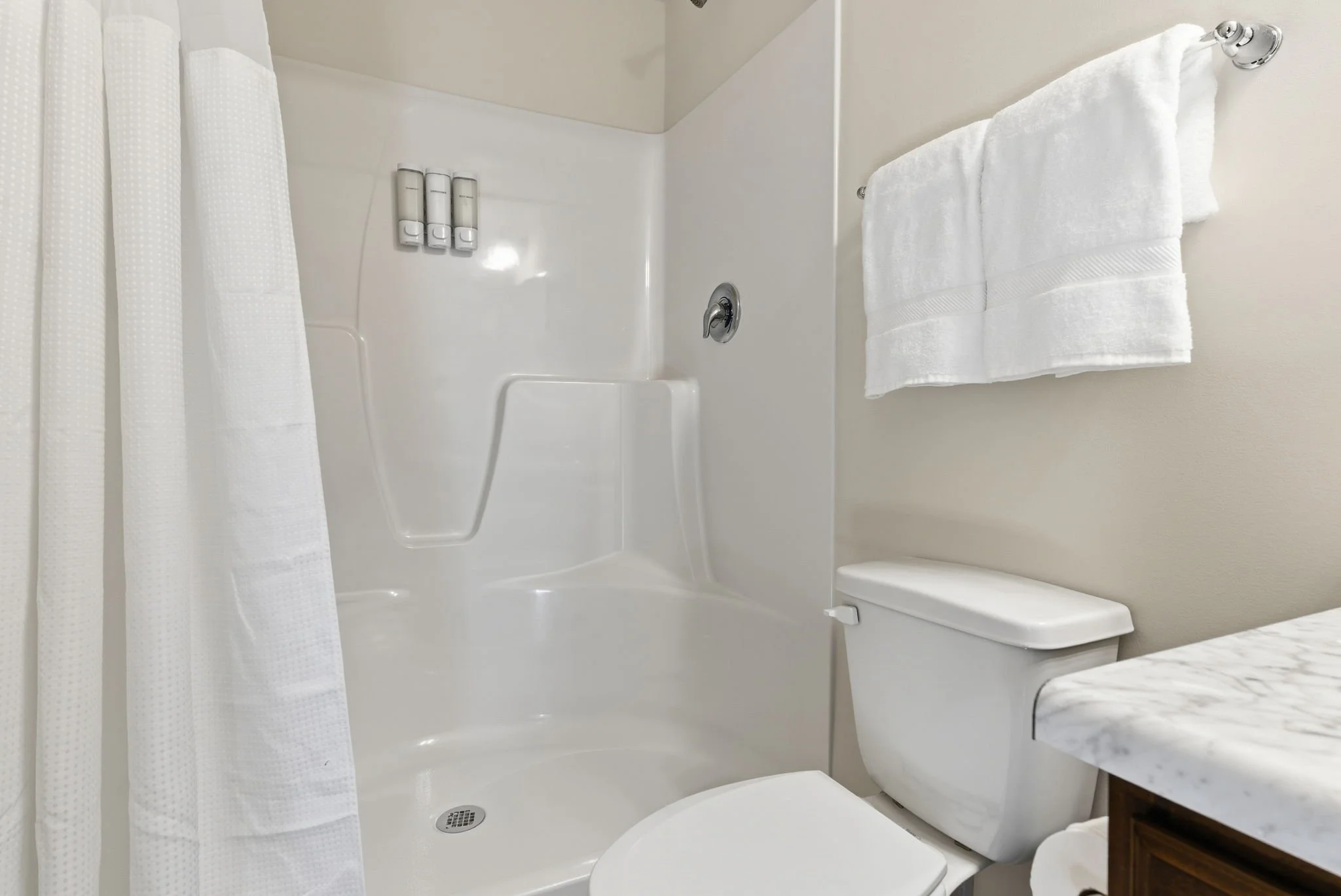 This full bathroom includes a large, sparkling clean shower with a wall-mounted soap dispenser (body wash, shampoo, and conditioner included). Designed for convenience and accessibility for all guests.