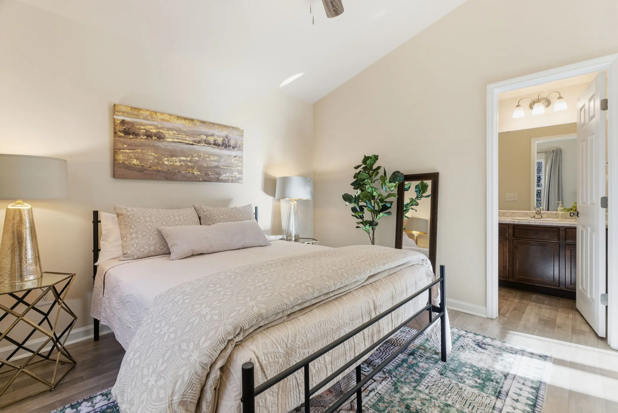 Rest easy in this spacious primary bedroom featuring a plush mattress, premium linens, and a vaulted ceiling. The room is styled with modern gold accents and abstract art, creating a boutique hotel feel for your stay in Durham.