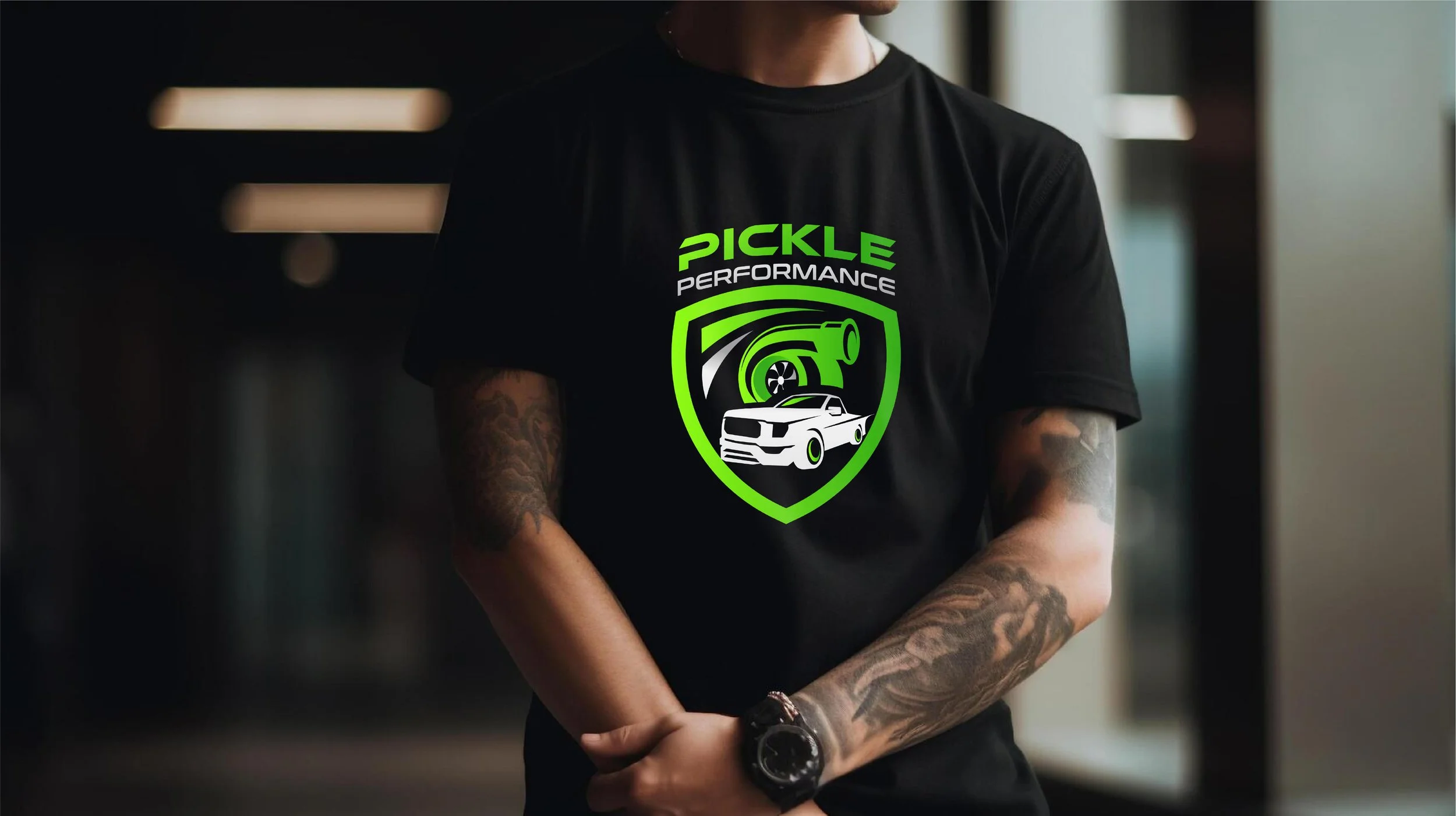 Person wearing a black T-shirt with a neon green and white logo featuring a car and a turbocharger, with the text 'Pickle Performance'