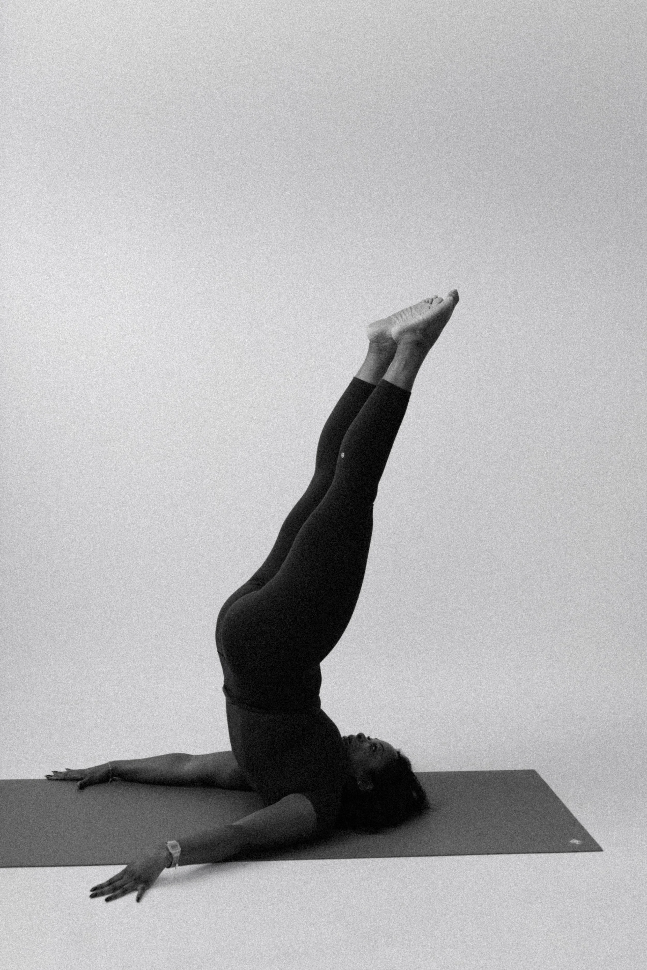 A person practicing pilates on a mat, performing a shoulder stand pose with legs extended upwards and hands supporting the back.