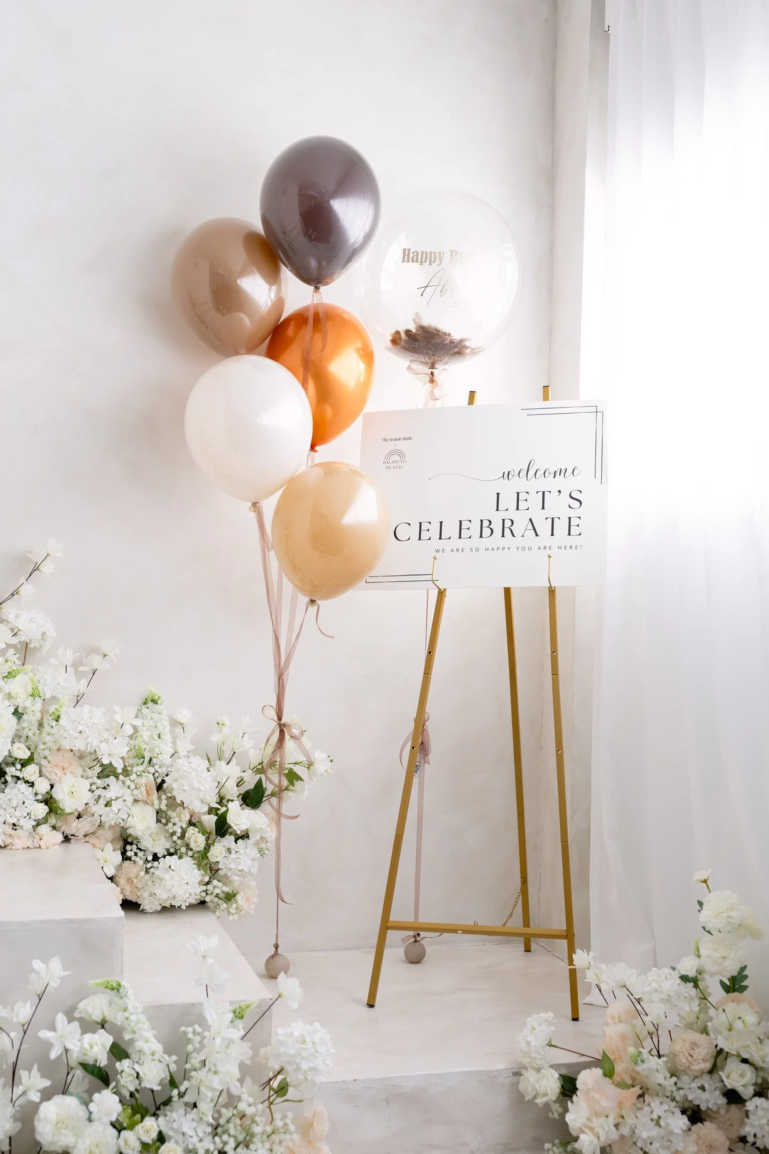 Private event decoration with balloons, floral arrangements, and a sign that says "Welcome Let's Celebrate".