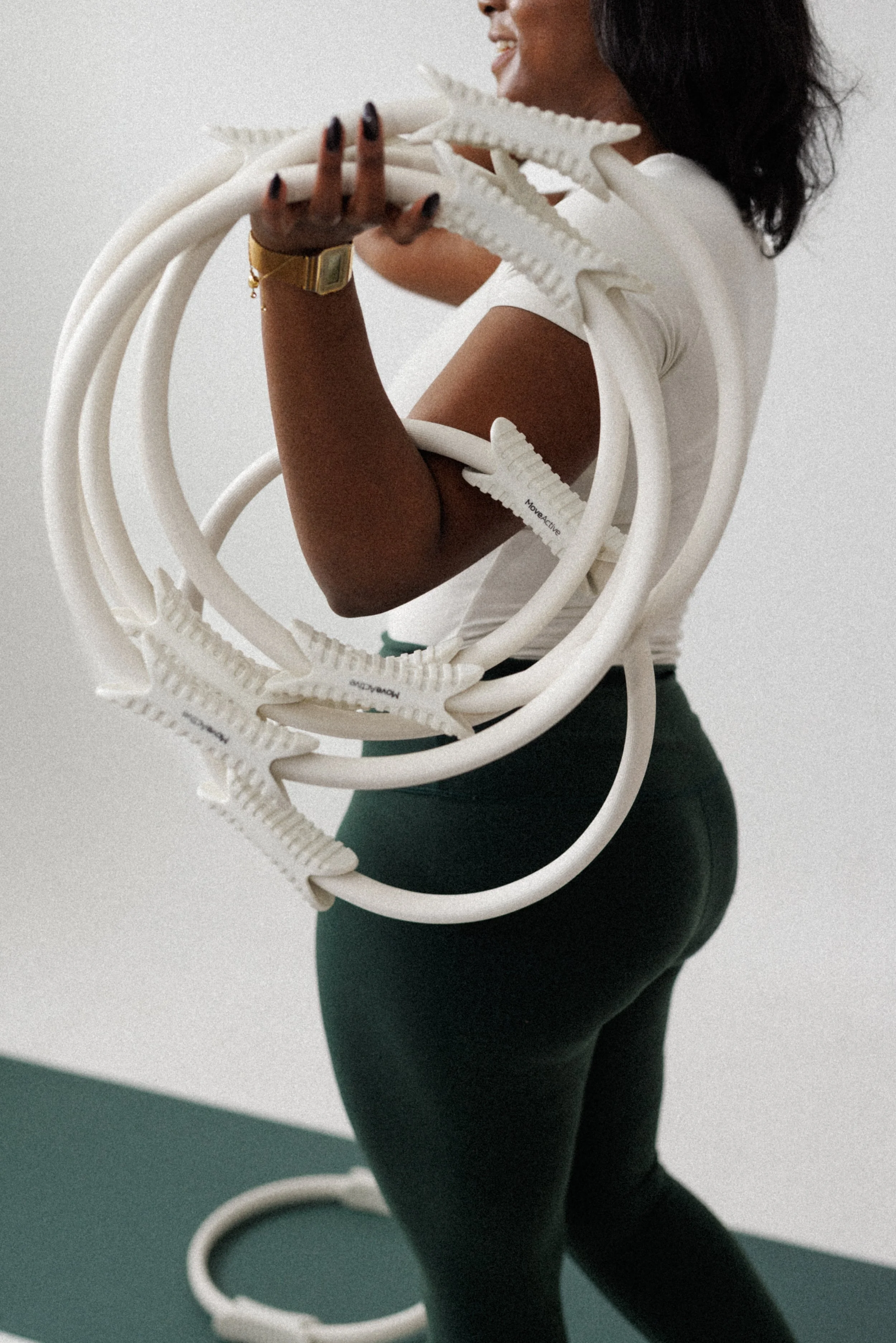 A woman holding several white starfish-shaped objects, smiling with her face partially visible, wearing a white top and black pants, with a gold watch on her wrist, standing against a plain light-colored background.