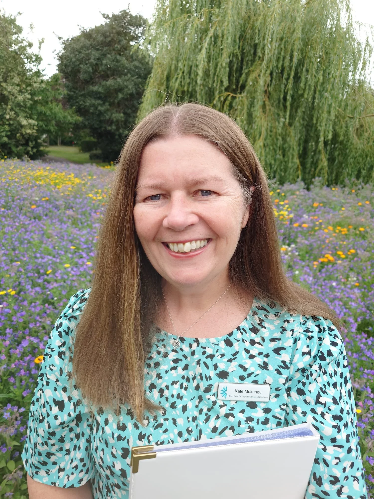 This picture of Kate was taken after a baby naming ceremony. Kate is wearing a pale turquoise patterned dress and a badge from the International College of Professional Celebrants.