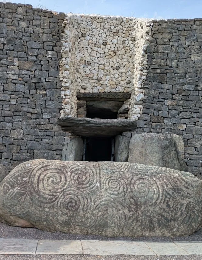 The image shows the Kerbstone in front of the entrance to Newgrange, in Brú na Bóinne, Co. Meath. The roof box, the exact point of the solar alignment is above the stone.