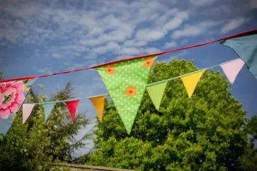 <img source='pic.gif' alt=' The link to Community Ceremonies page is an image of multicoloured bunting with a backdrop of green trees and bright blue sky. ' />.