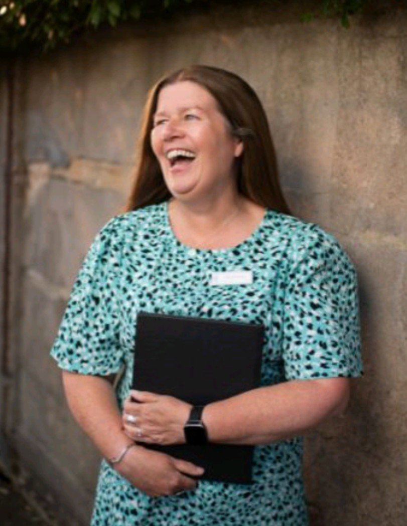 This picture was taken in an urban setting by a professional photographer. In it, Kate is wearing a celebrant badge on a green dress and she is laughing.