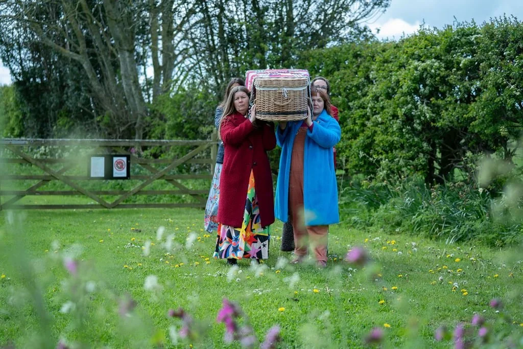 Four women, one of whom is Kate, carry a wicker coffin at a North East Natural Burial Site, Seven Penny Meadow