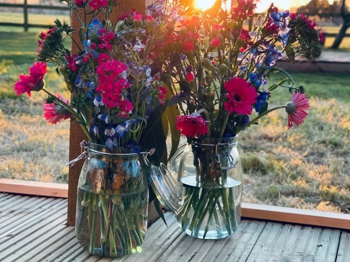 This image shows two glass jars filled with freshly picked flowers..  Photo by Elizabeth Dunne on Unsplash