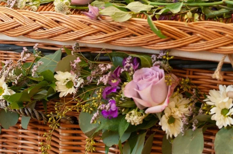 This is an up close image of a willow coffin which has flowers attached. It is from the Good Funeral Guide and is available on Unsplash.