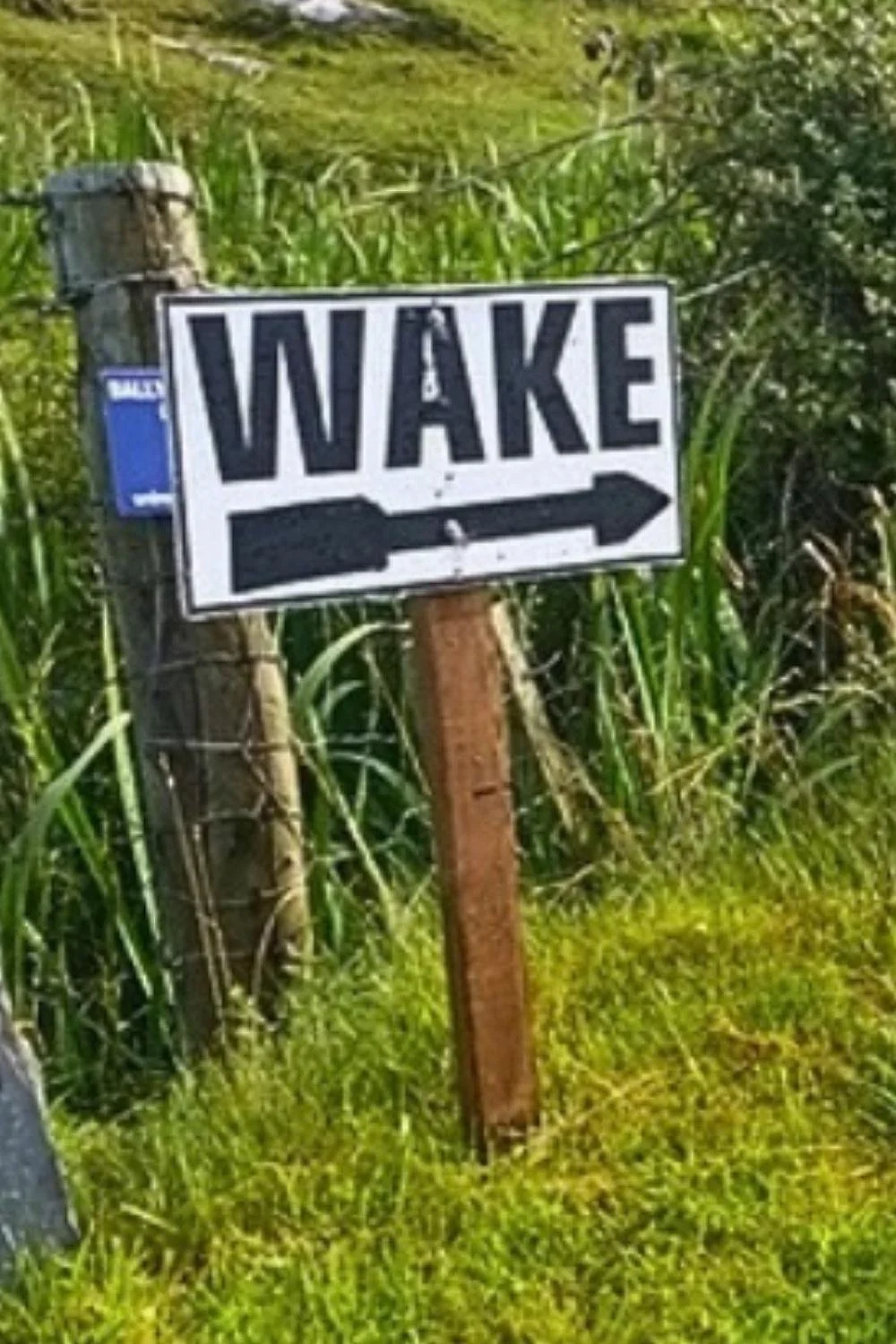 There sign at the side of a road says "wake" is common in rural Ireland to direct mourners to the house where they can visit the dead person and their family and friends.