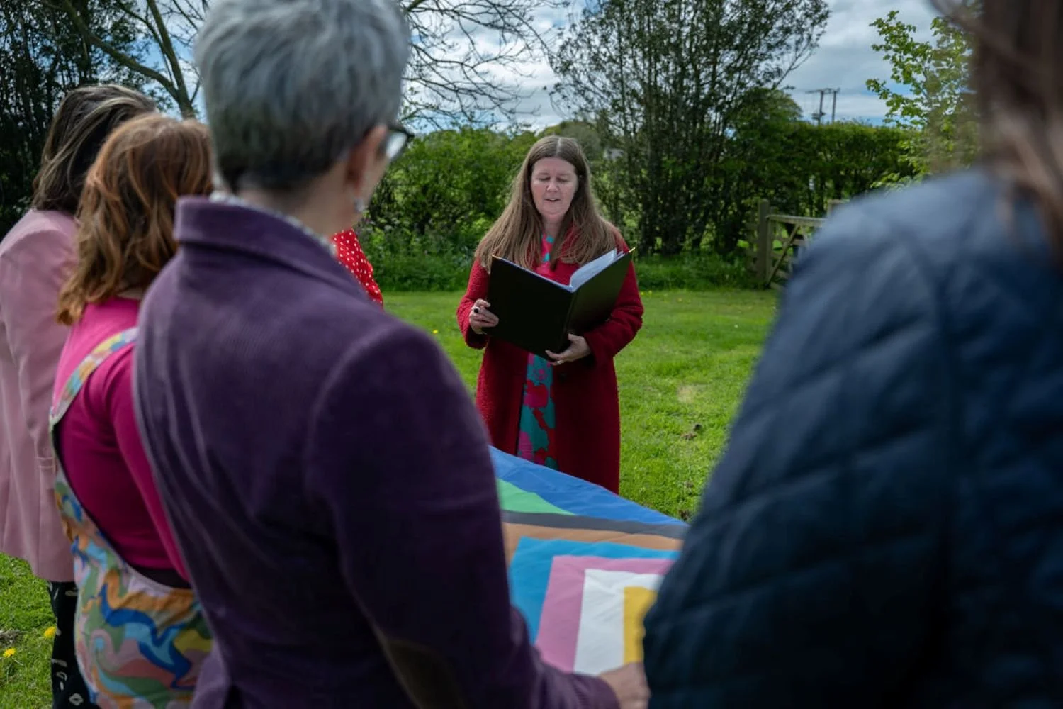 Kate is reading from a ceremony script to people stood behind a coffin draped in a pride flag.