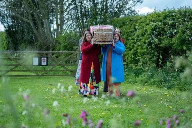 Four women, one of whom is Kate, carry a wicker coffin at a natural burial site in North East England called Seven Penny Meadow