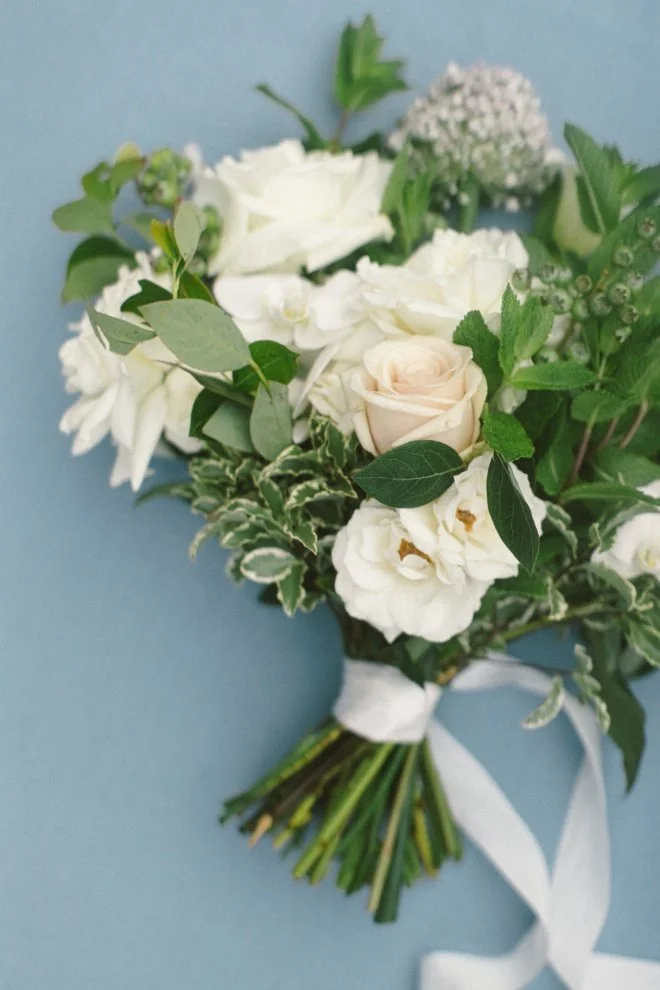 A bunch of white flowers set against a blue background as a white ribbon tied around the stems.