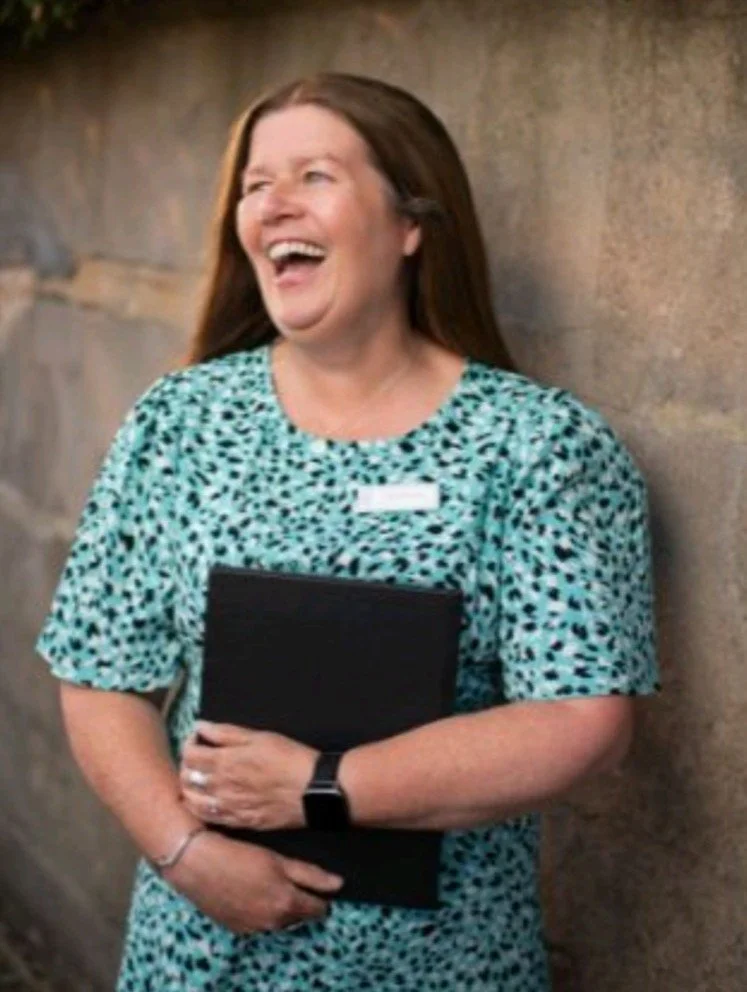 This picture of Kate was taken in an urban setting. She is holding a black notepad, looking away from the camera and laughing.