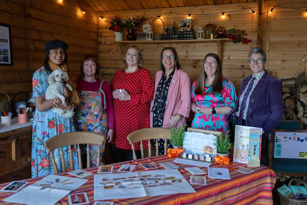 Six women stand in a row smiling. In front of them is a table with end of life planning materials