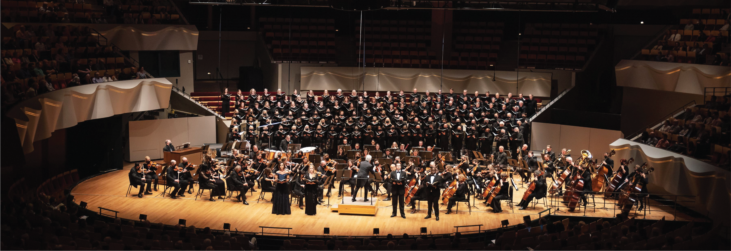 Orchestra and choir performing on a stage in a concert hall with a full audience.