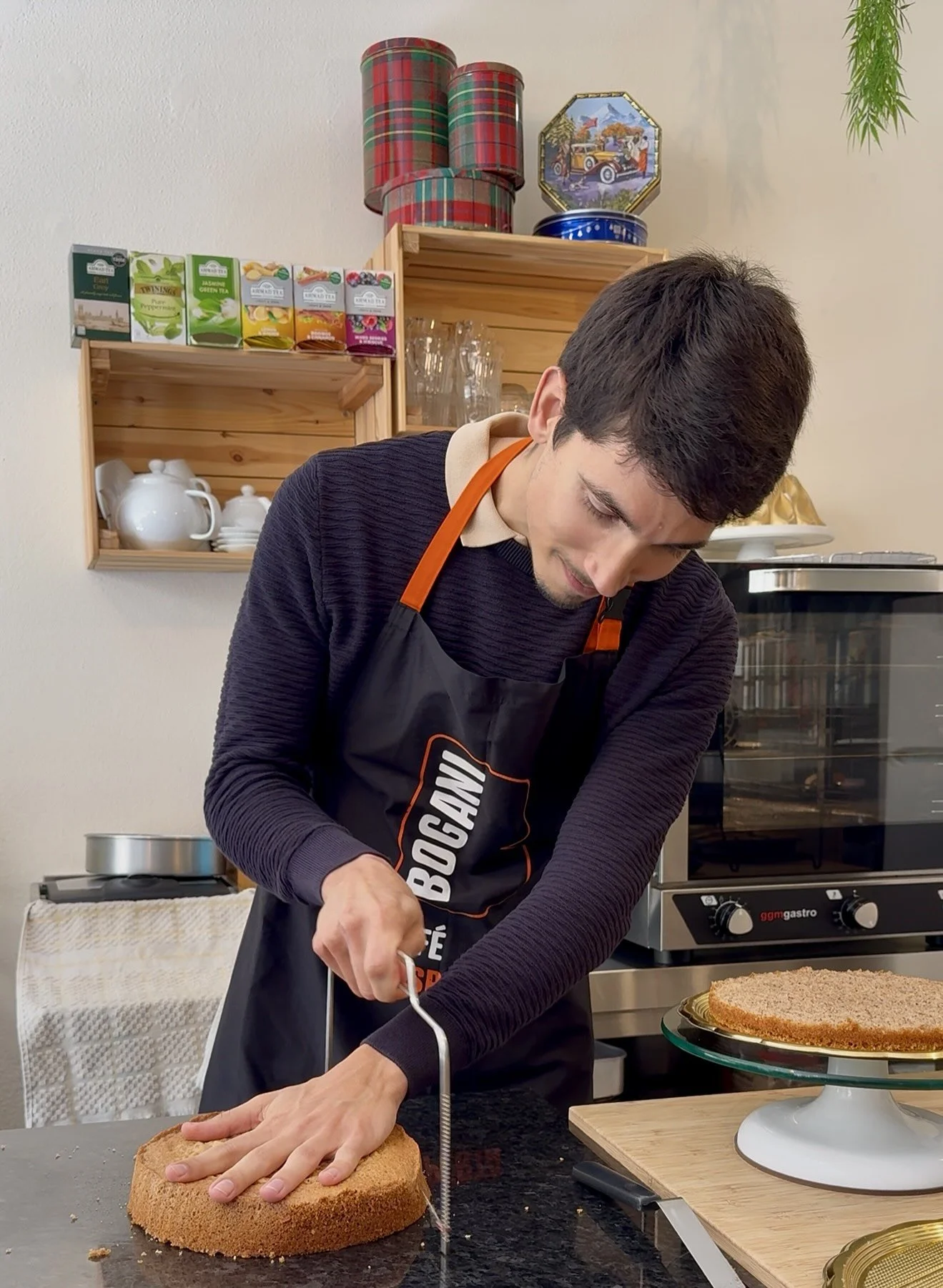 A man slicing a round cake with a wire cutter in a kitchen.