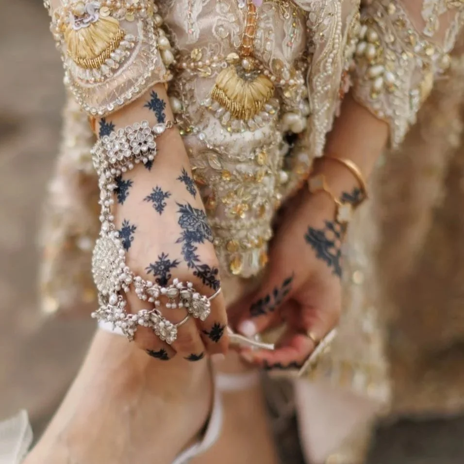 Close-up of hands and arms decorated with henna designs, jewelry, and traditional attire, likely for a special occasion like a wedding.