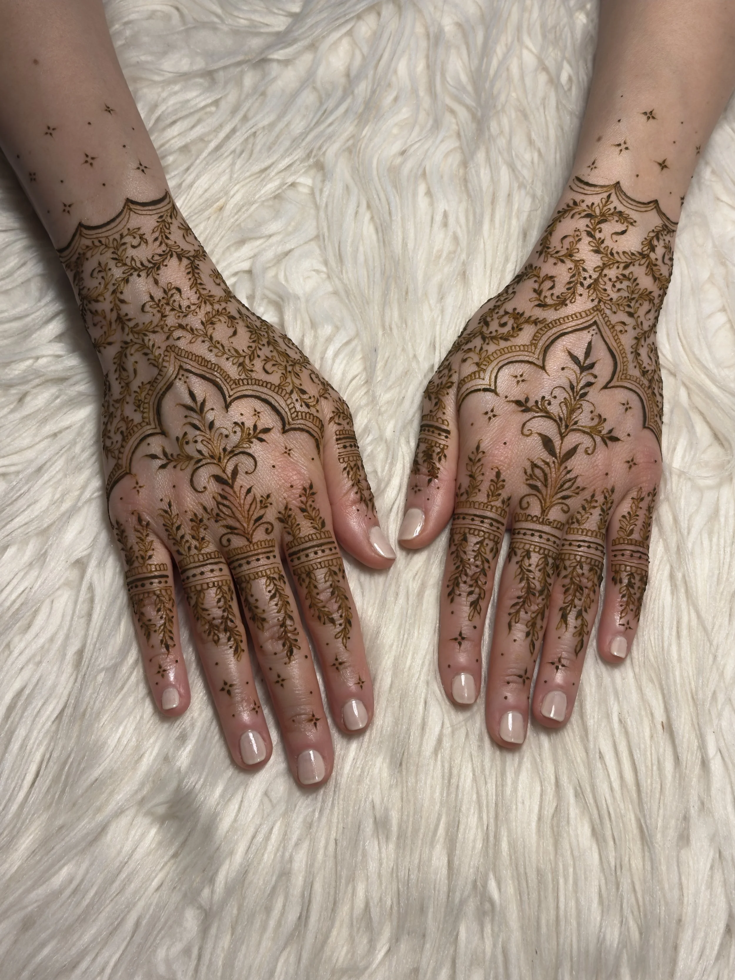Close-up of bride’s hands with minimal dome bridal henna design and pearl detailing, holding a bespoke tealight candle matching her green and lavender bridal outfit. Bridal necklace subtly visible in the background.