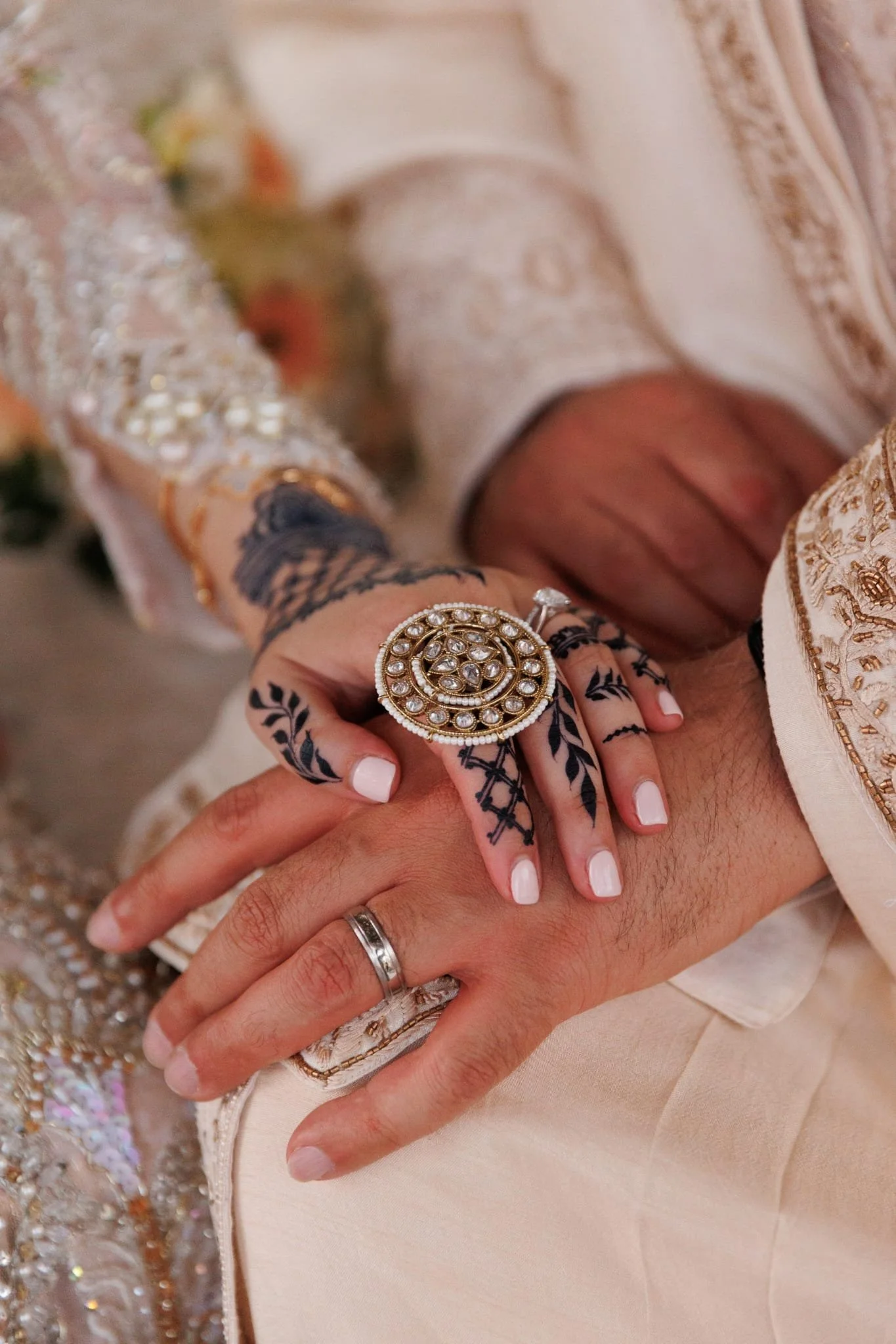 Close-up of a couple's hands during a wedding ceremony, holding each other with jewelry and traditional attire.