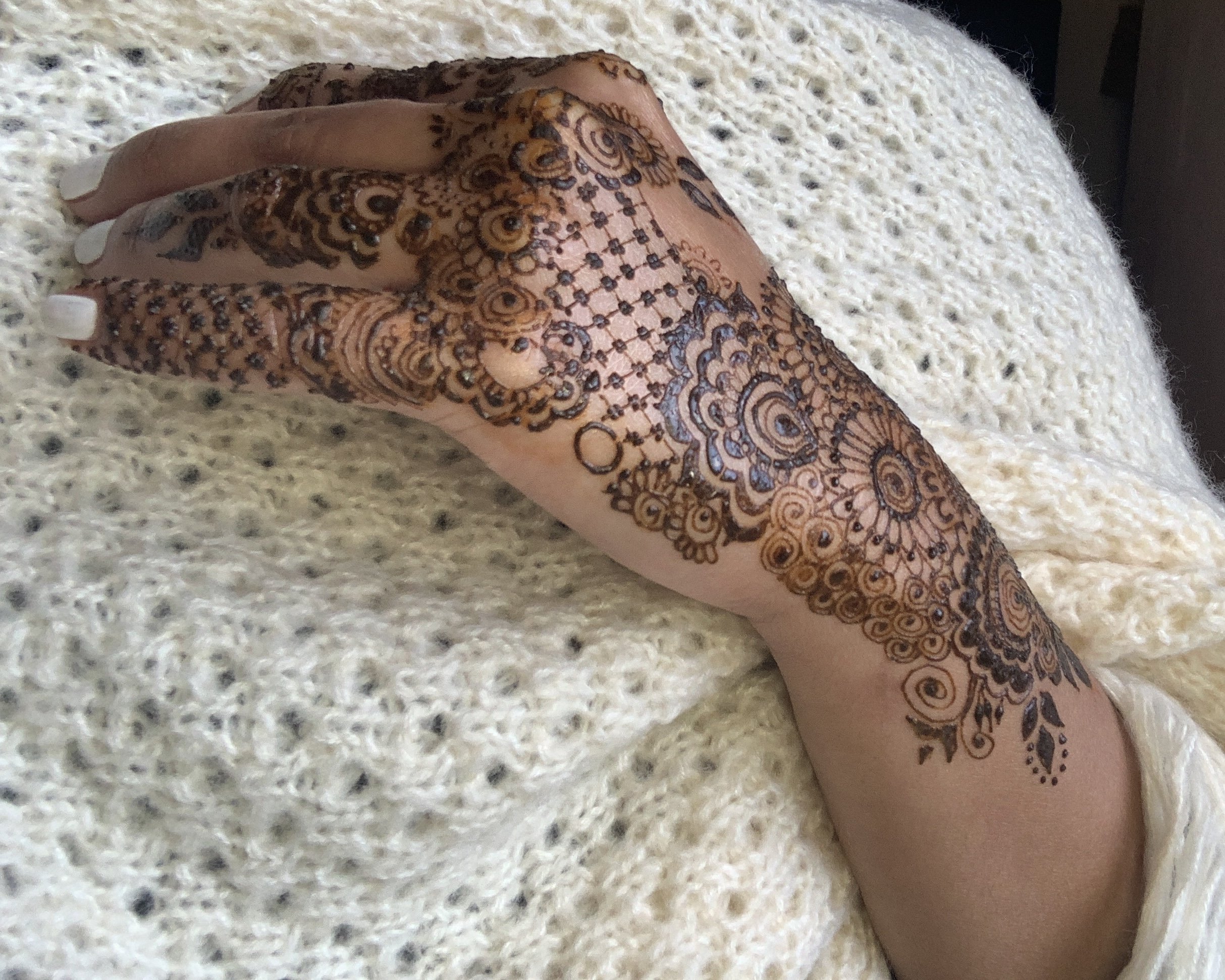 A hand with intricate henna designs resting on a cream-colored knitted blanket.