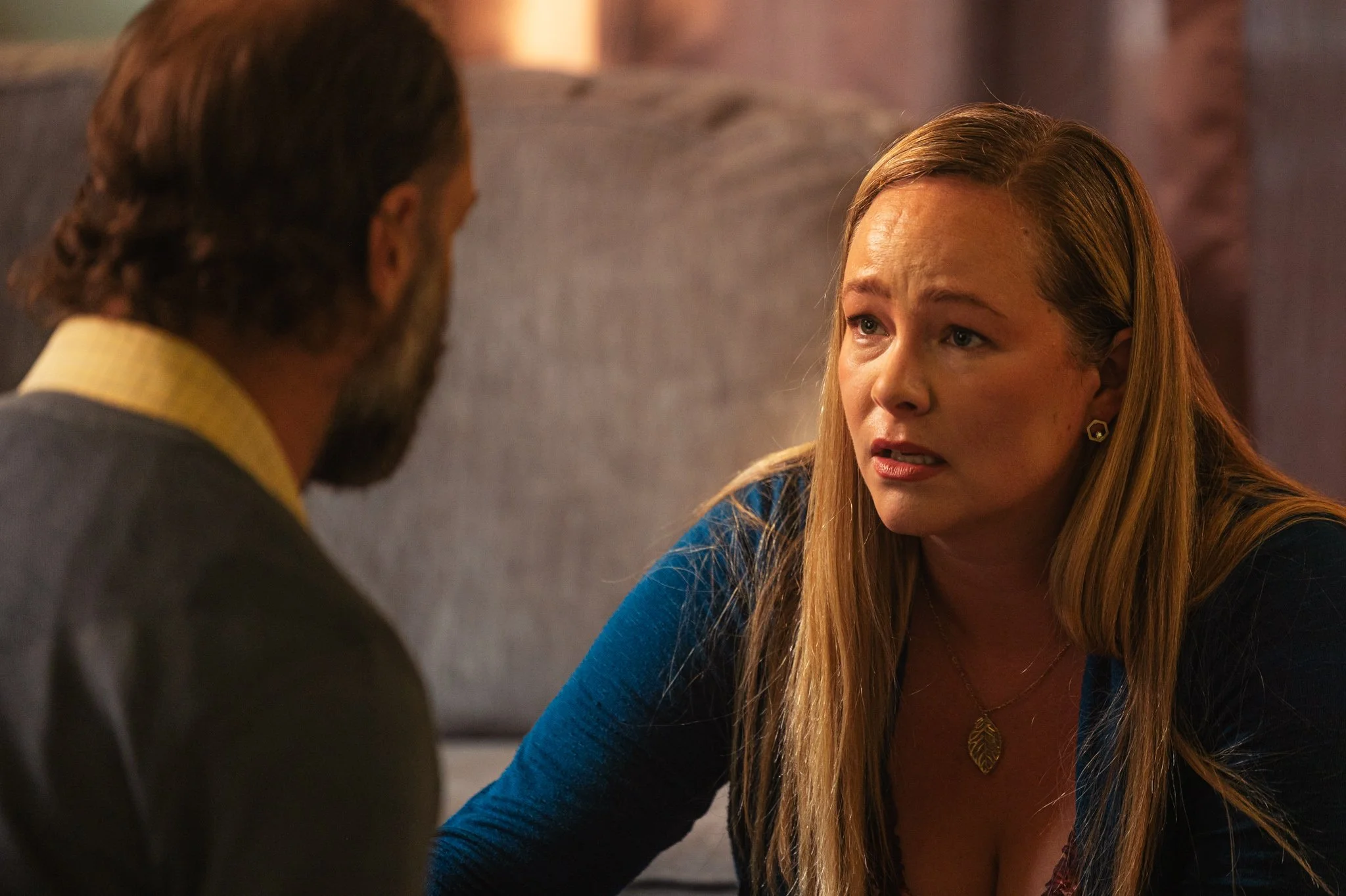 A womand and man kneeling on the floor in an emotional sitauation. The woman has straight blonde hair and is wearing a teal top. The man is facing away from the camera. He has a beard and a shirt with yellow collar.