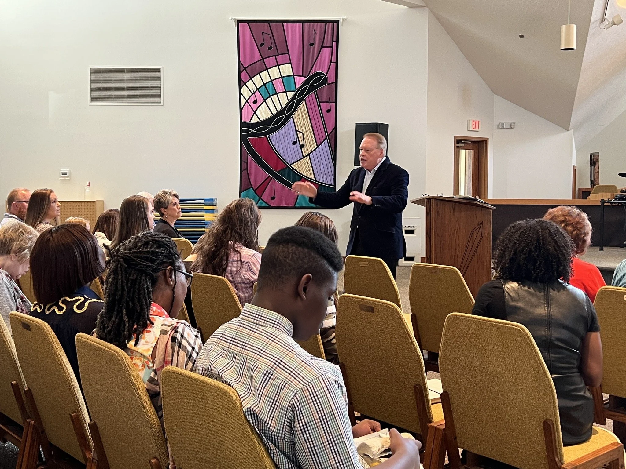 man preaching to a congregation inside a church with stained glass windows