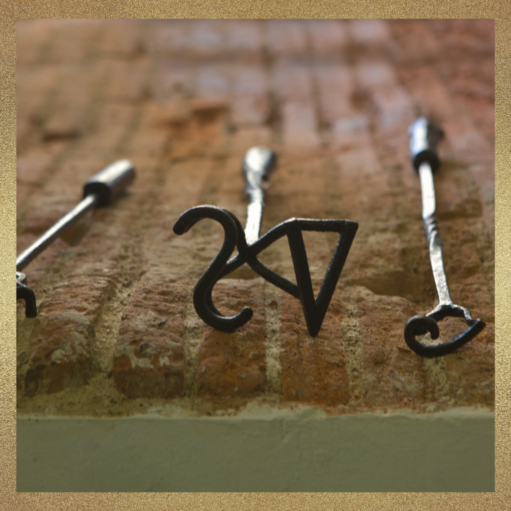 Three iron cattle branding irons resting against a textured brick wall, symbolizing how marks of ownership and identity are impressed by others — a metaphor for reputation and perception.