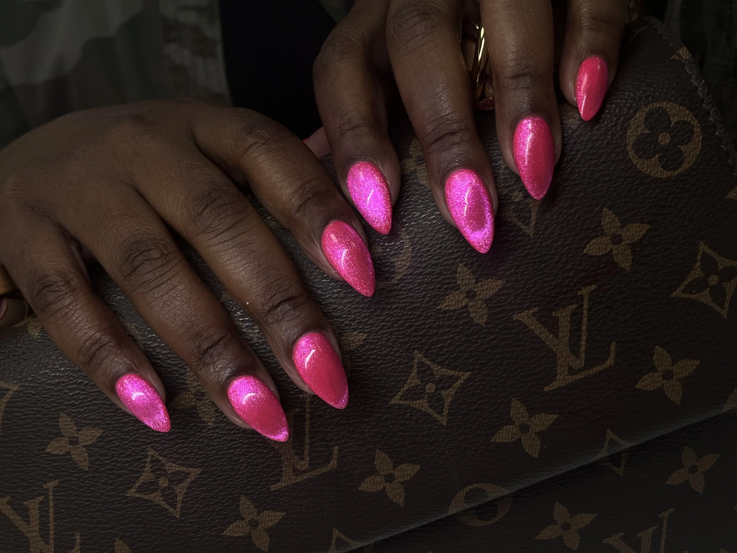 Close-up of hands with pink glittery almond-shaped nails resting on a Louis Vuitton handbag.